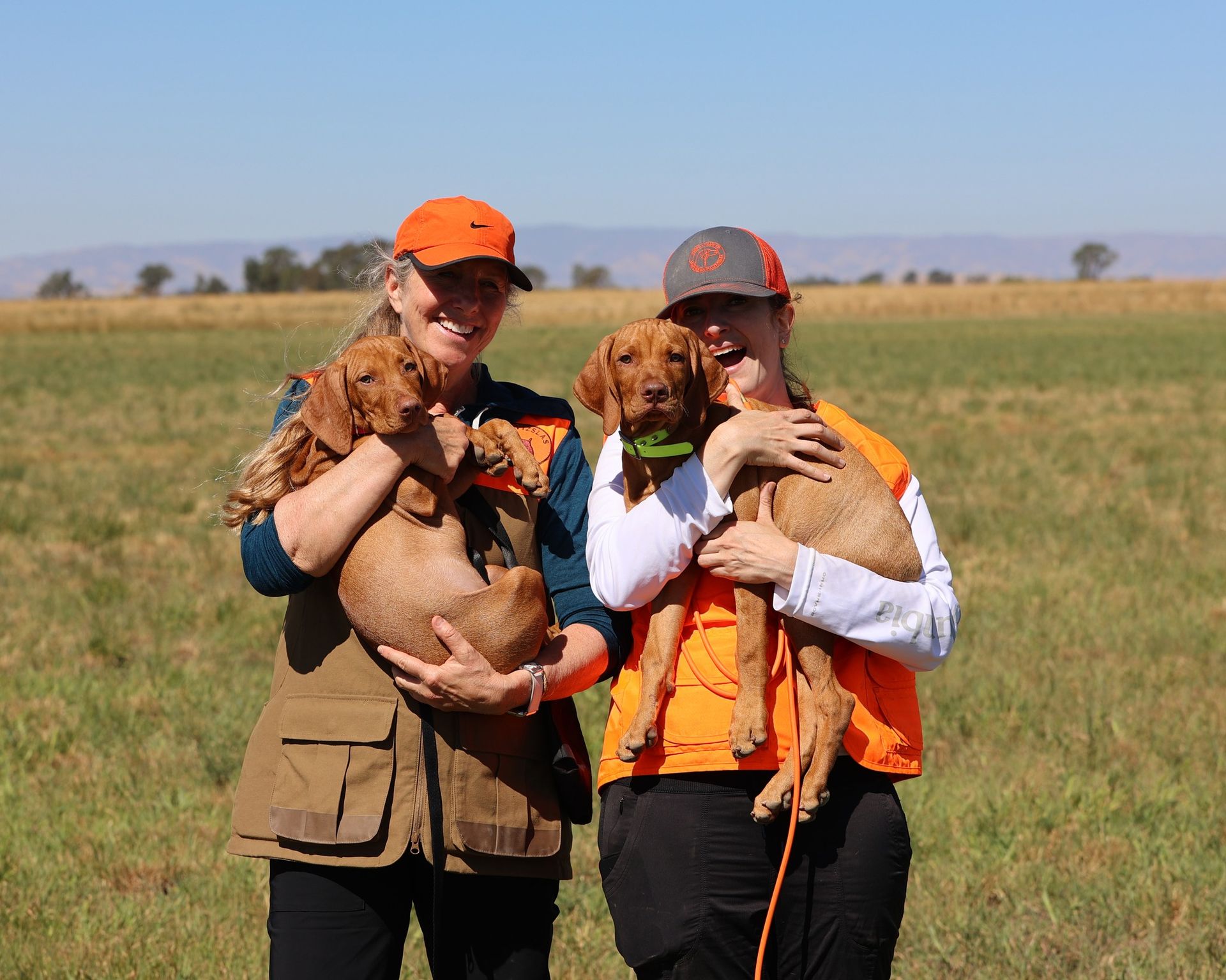 Two women are holding two dogs in a field.