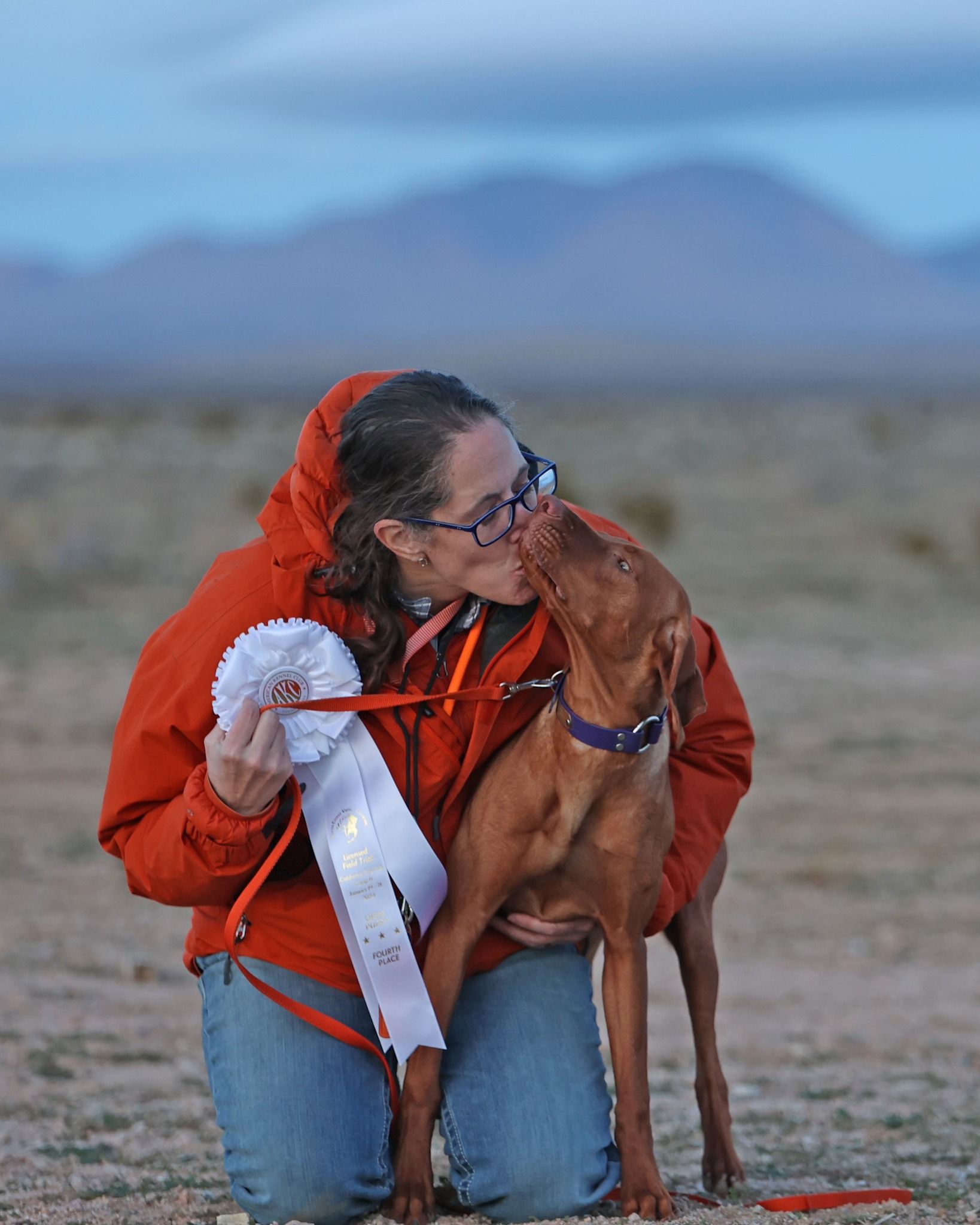 A woman kissing a dog while holding a ribbon