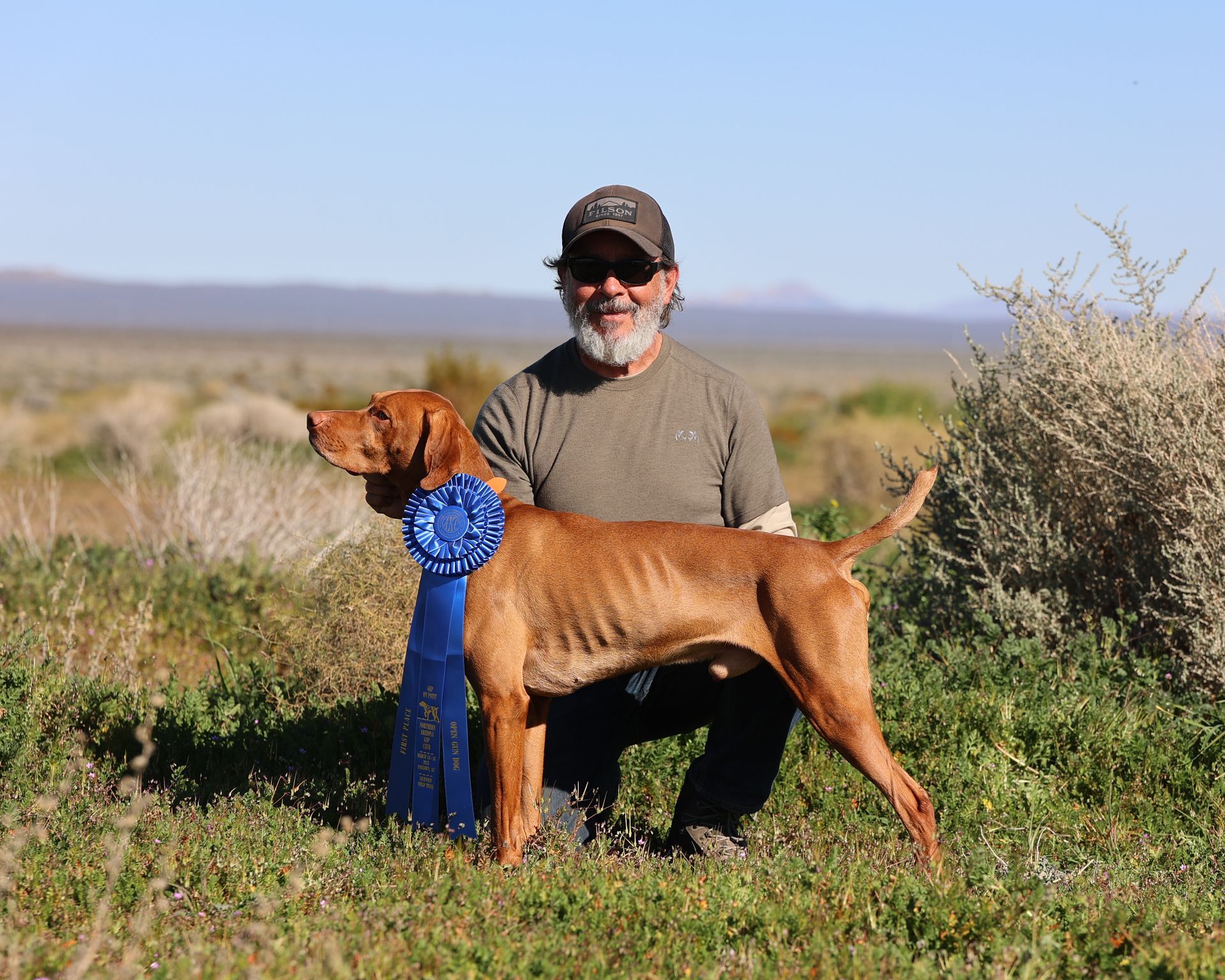 A man is kneeling down next to a dog in a field.