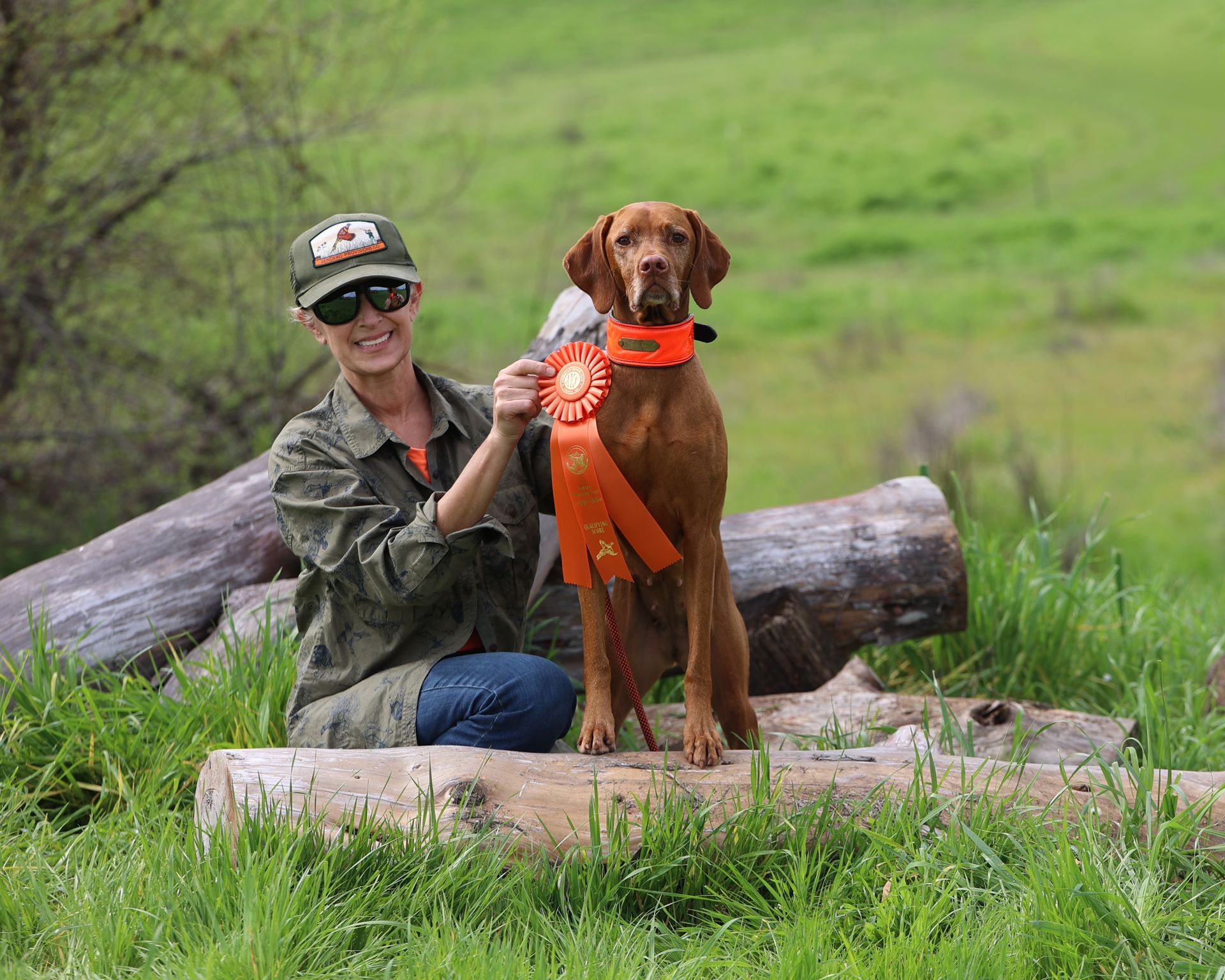 A woman is kneeling down next to a dog holding two ribbons.