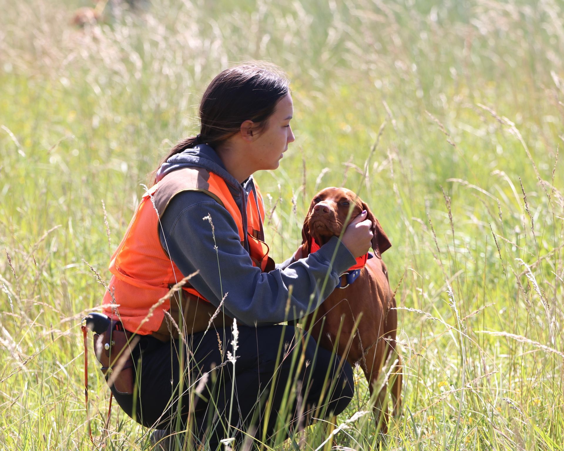 A woman is kneeling down with a dog in a field.