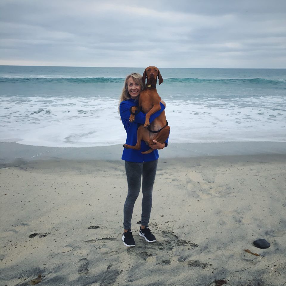 A woman is holding a brown dog on the beach