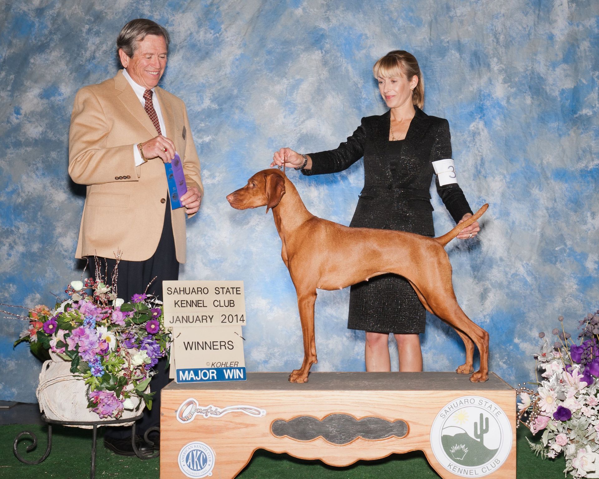 A man and a woman standing next to a dog with a sign that says vax-nm on it