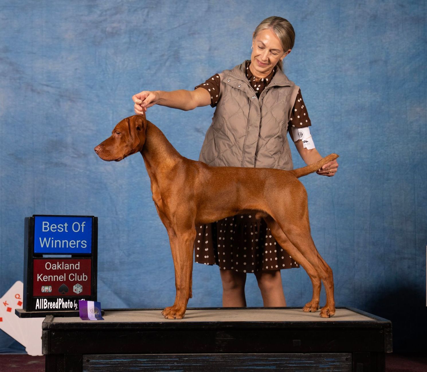 A woman is holding a dog in front of a sign that says best of winners