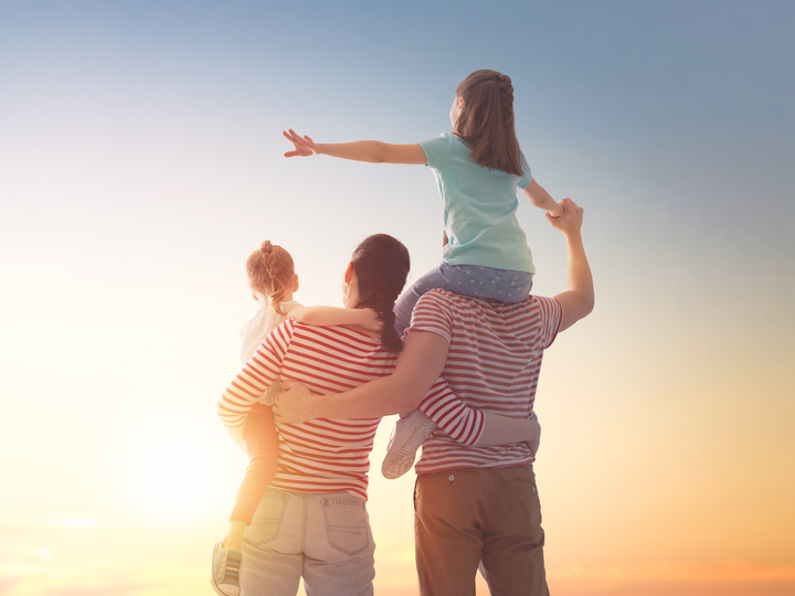 Family running on a beach at sunset; woman, man, and child splashing in the water.