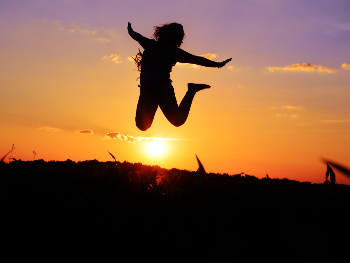 A silhouette of a person jumping with arms outstretched against a vibrant orange and purple sunset.
