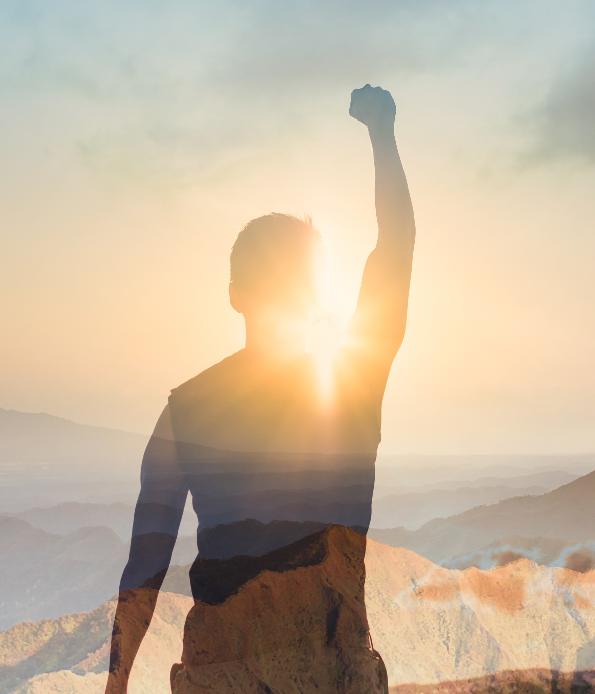 Man with raised fist, silhouetted against a bright sunset over a mountain range.