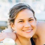 A person smiling warmly in a close-up portrait, seen outdoors with soft, out-of-focus background lighting.