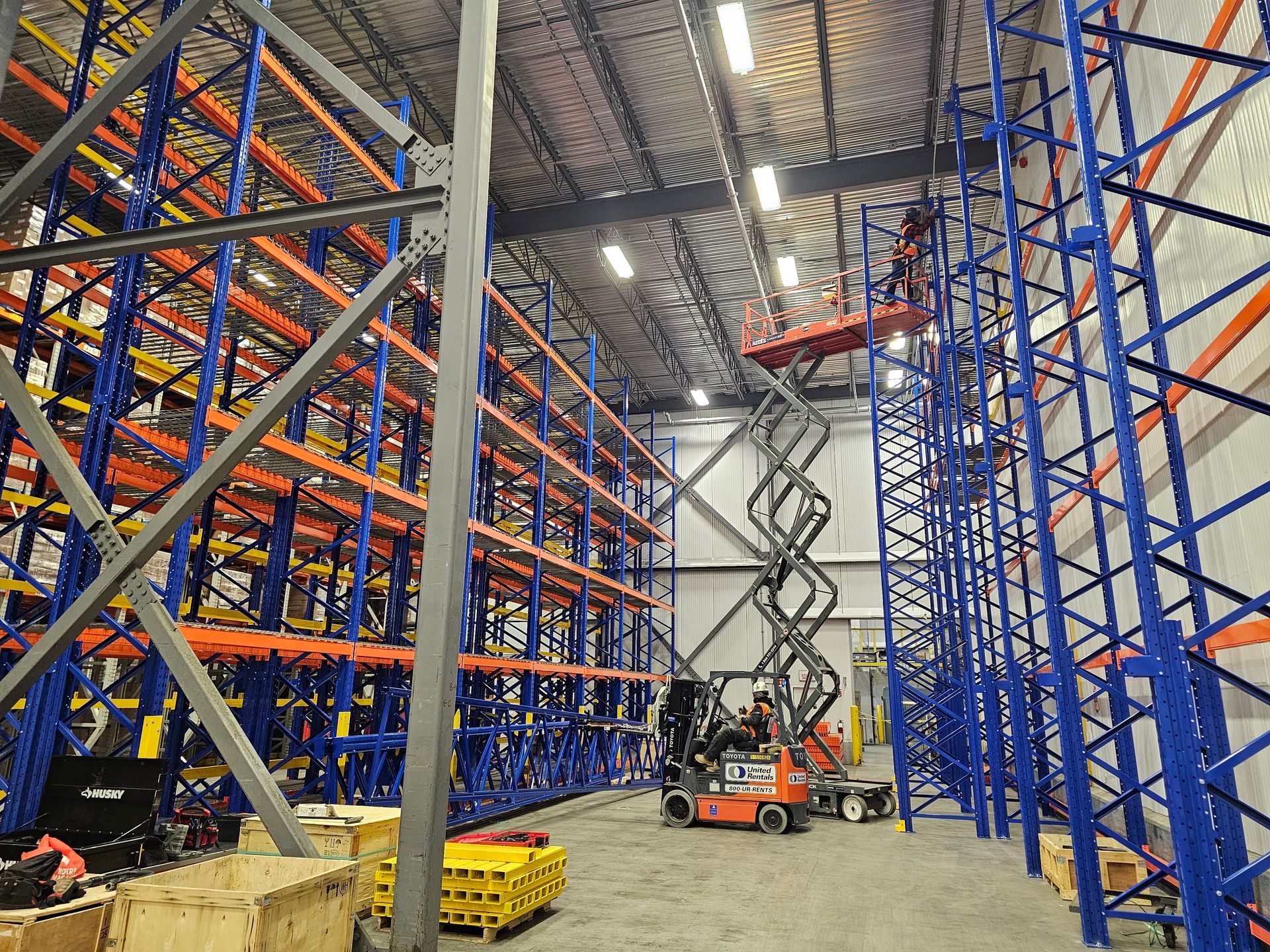 Racking installation services inside warehouse with tall blue and orange racking, with workers on a lift.
