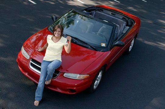 Una mujer está sentada en la parte delantera de un coche rojo descapotable.