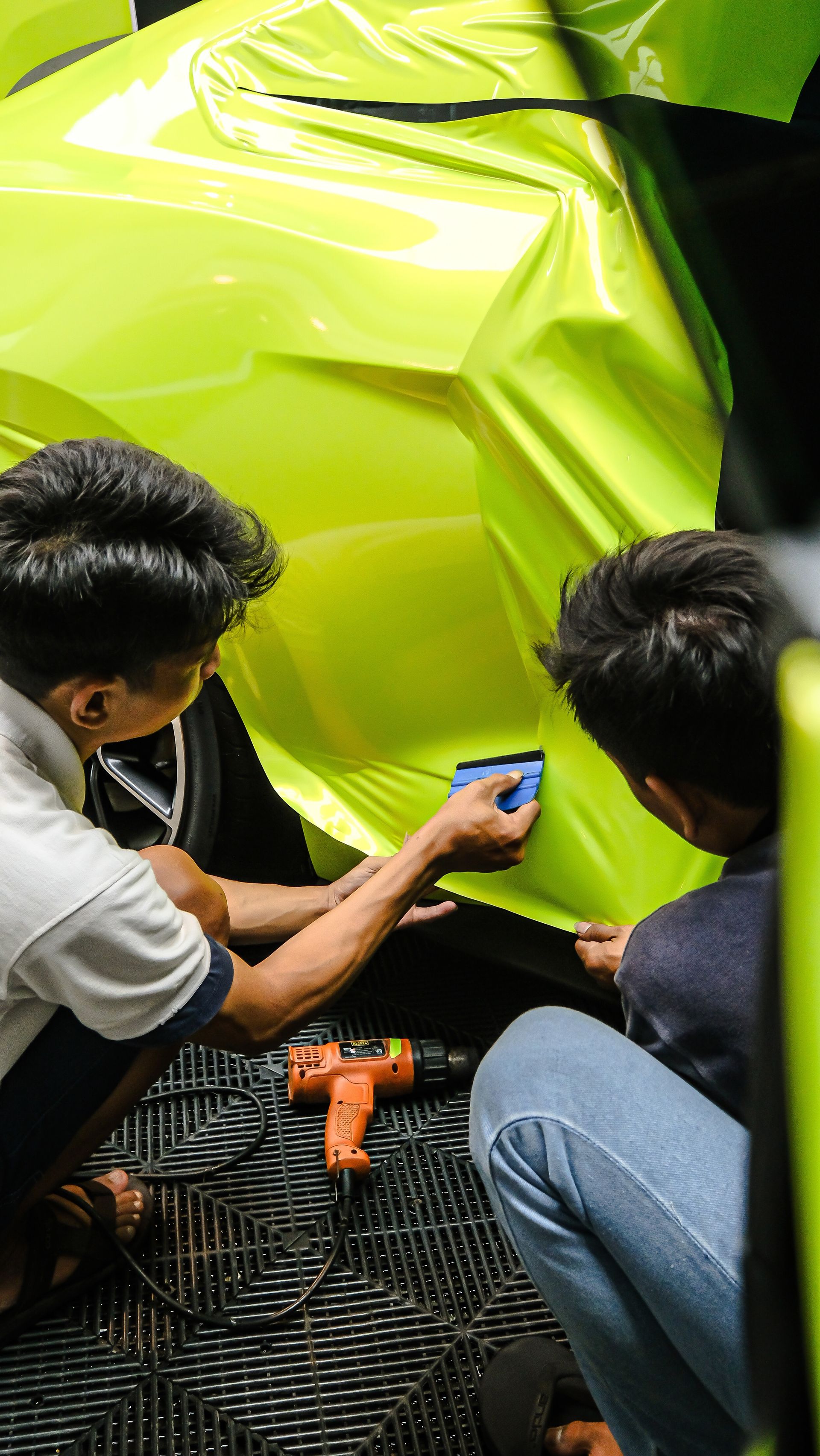 Two people applying neon yellow vinyl wrap to a vehicle. One holds a tool, the other uses a squeegee.