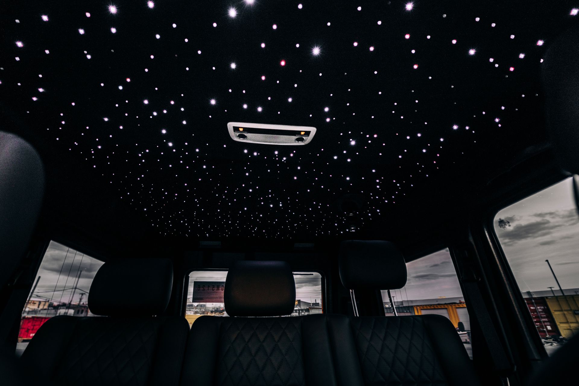 Black car interior with illuminated starlight headliner, seen from the backseat, with black seats.