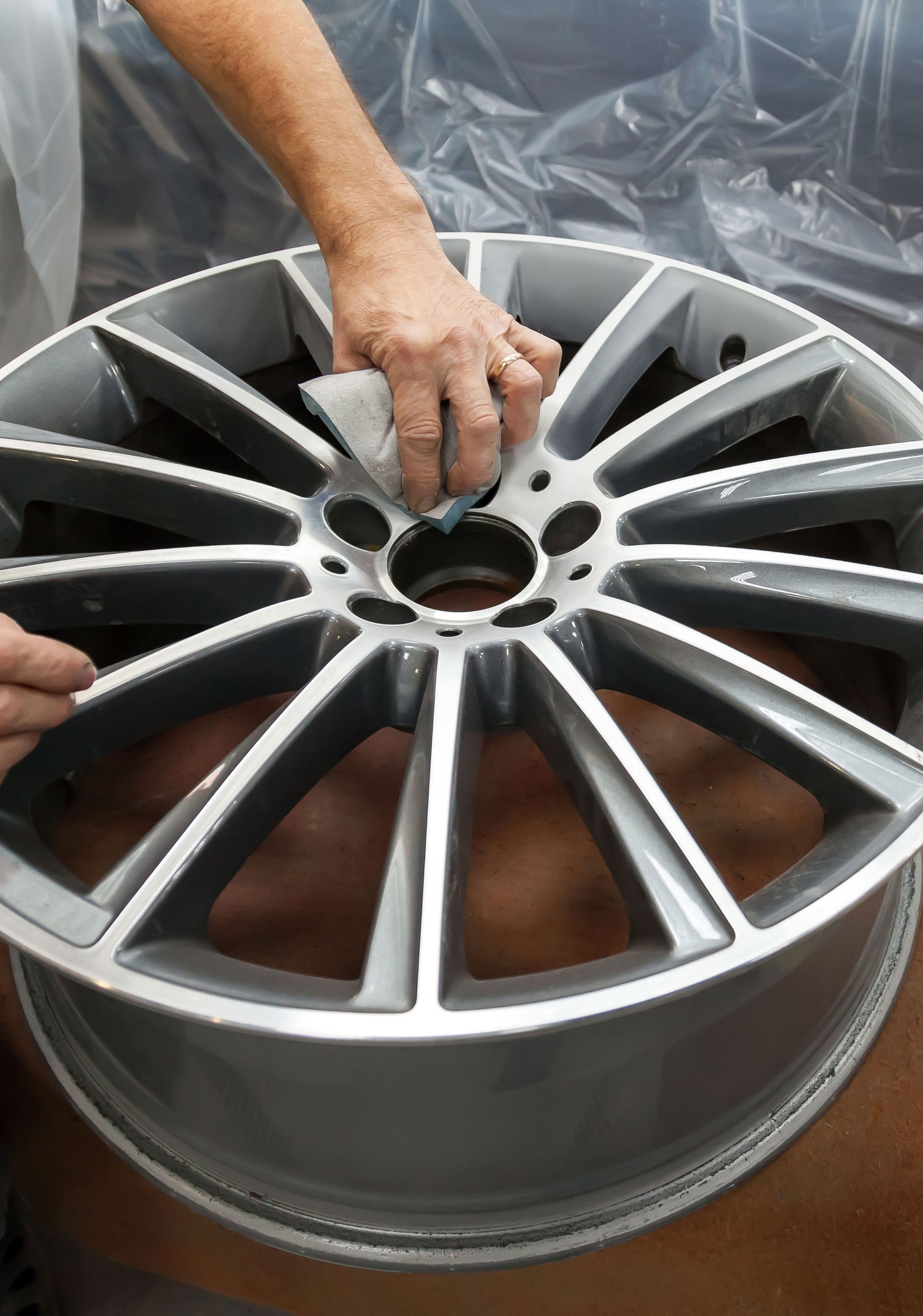 Person sanding a silver alloy wheel.