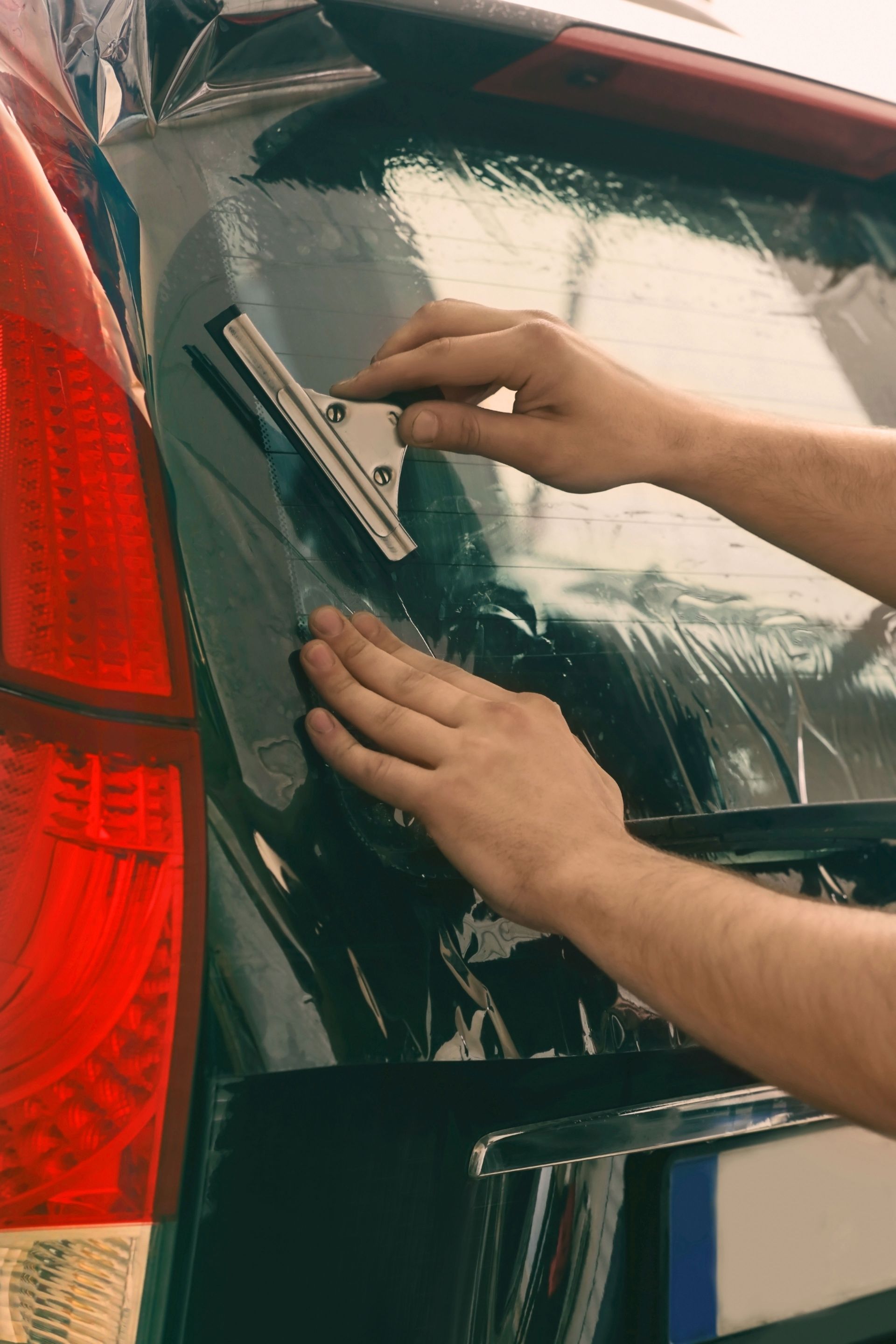 Person spraying blue film on a black car windshield with a spray bottle.