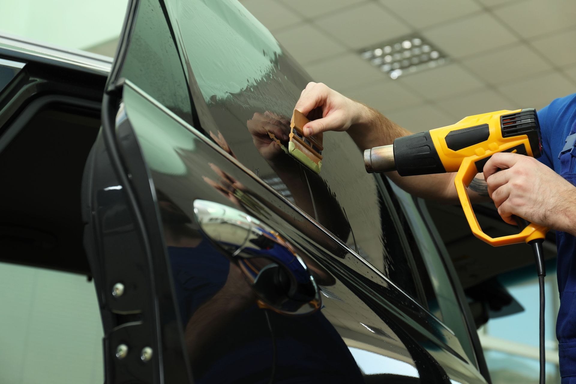Person applying tinted film to a car window with a heat gun.