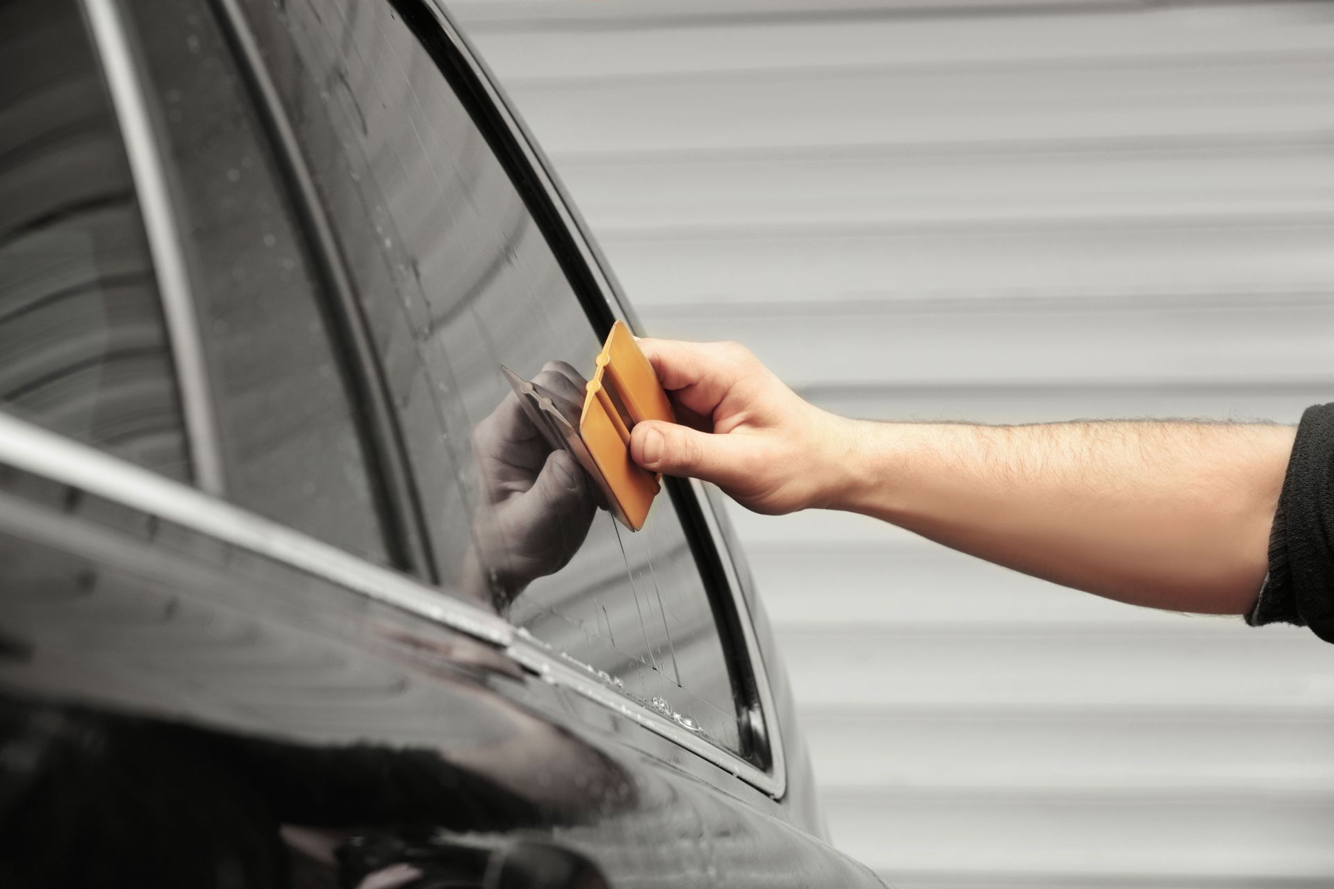 Person applying tint film to a car window with a squeegee.