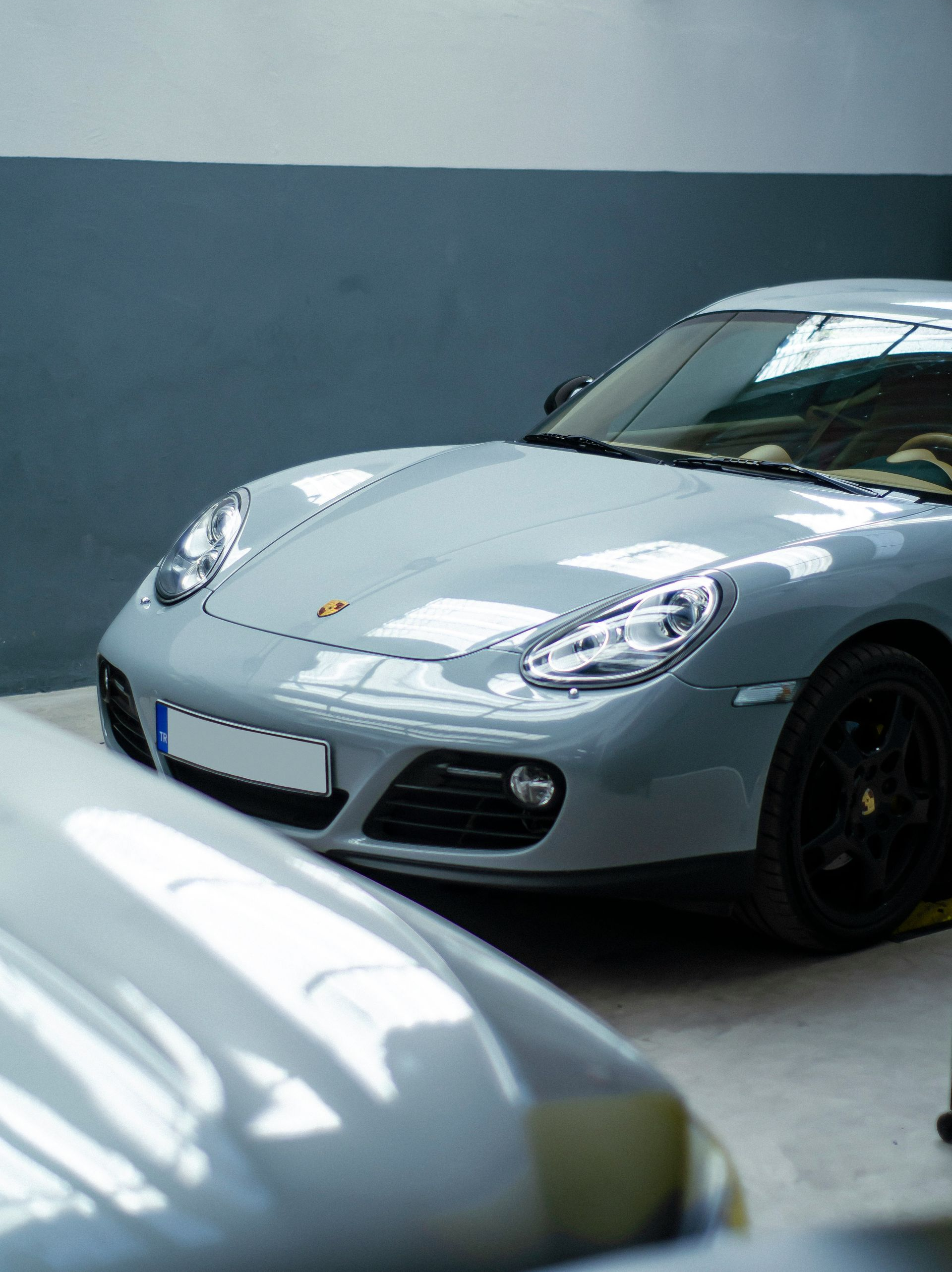 Gray Porsche sports car parked in a garage with another car partially in view.