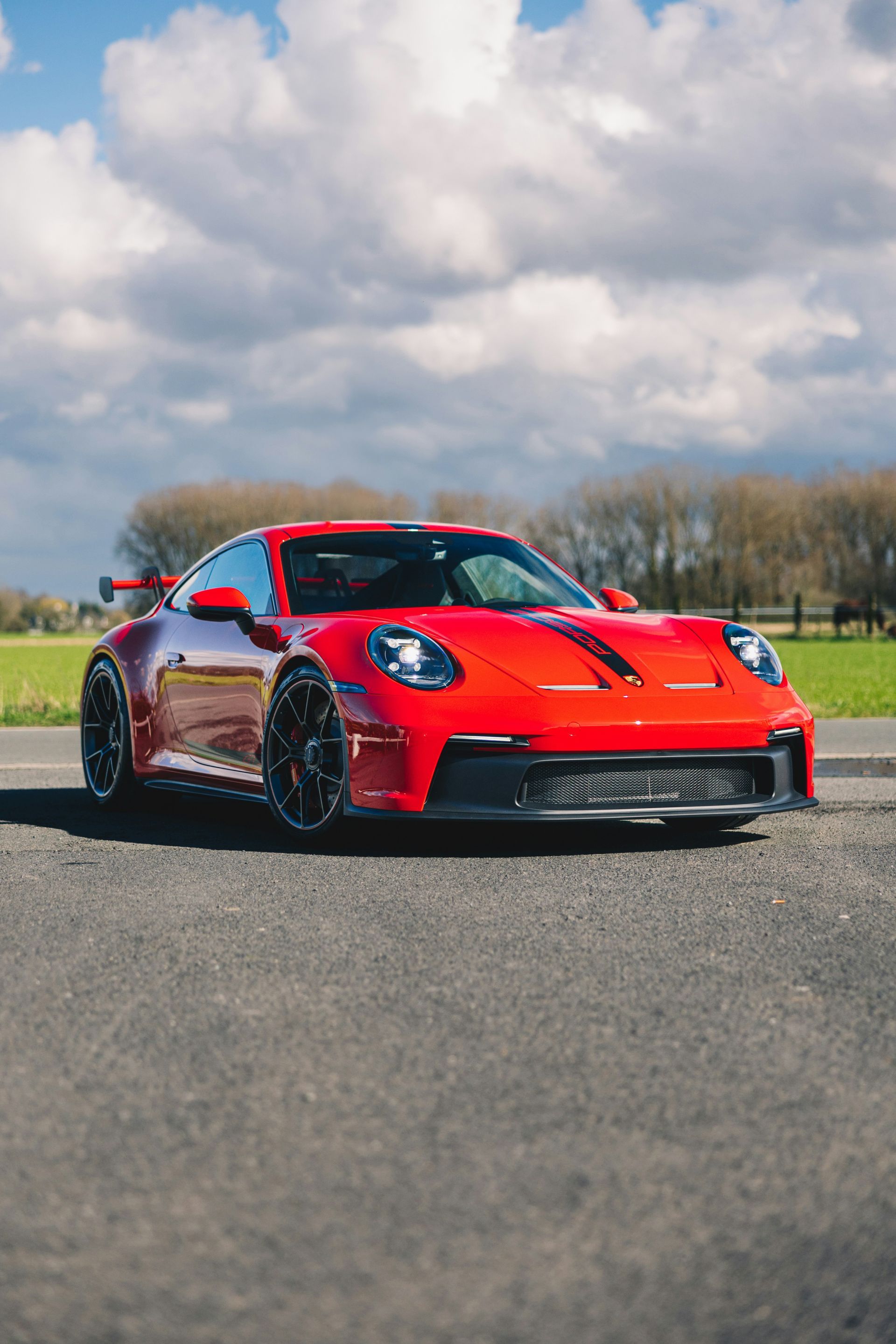 Red Porsche 911 GT3 sports car parked on a road with a cloudy sky in the background.
