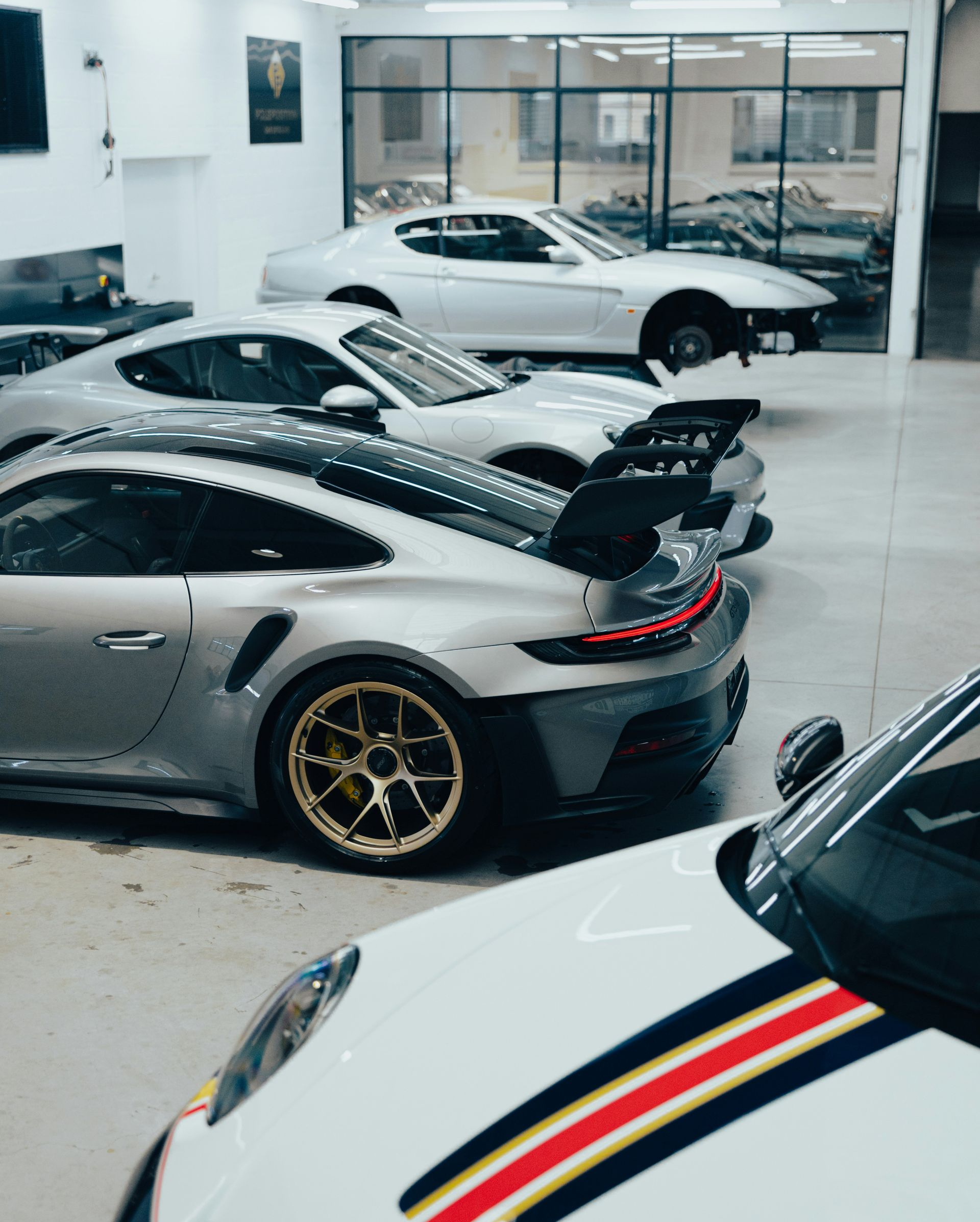 Silver and white sports cars parked in a garage, some with racing stripes and spoilers.