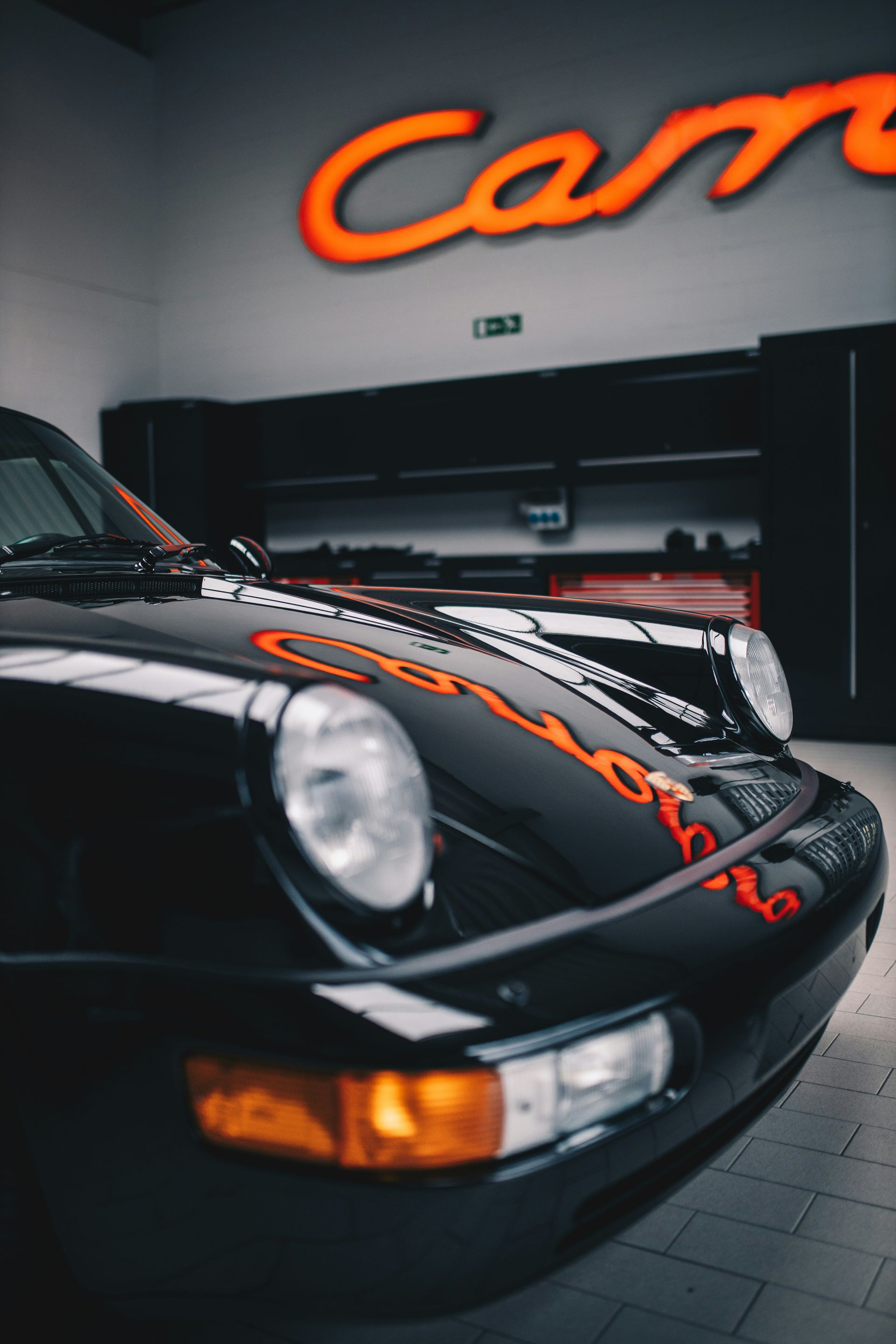 Black Porsche sports car in a bright white garage, rear view, large spoiler, professional detailing setting.
