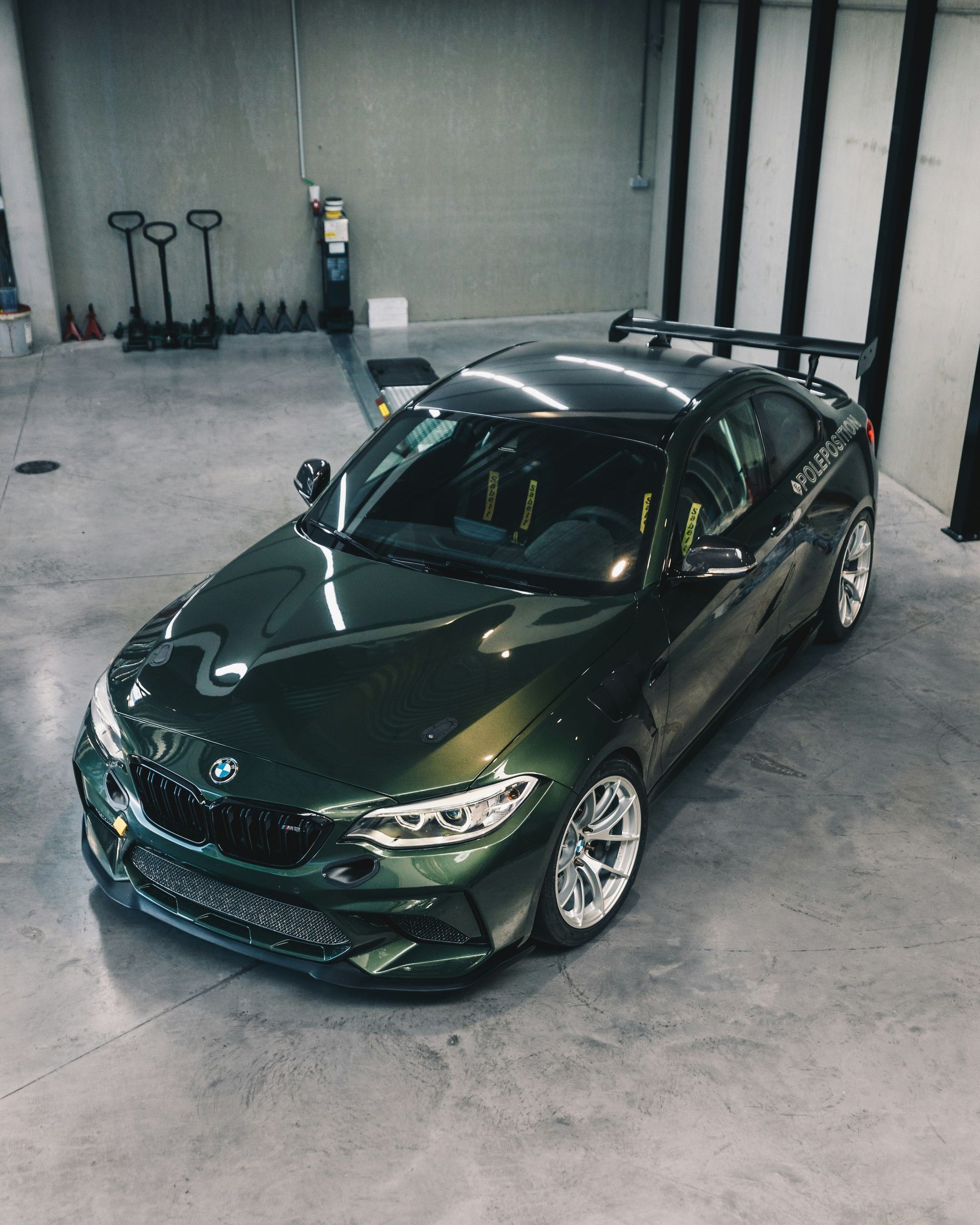Green BMW coupe with a rear wing, parked in a garage.