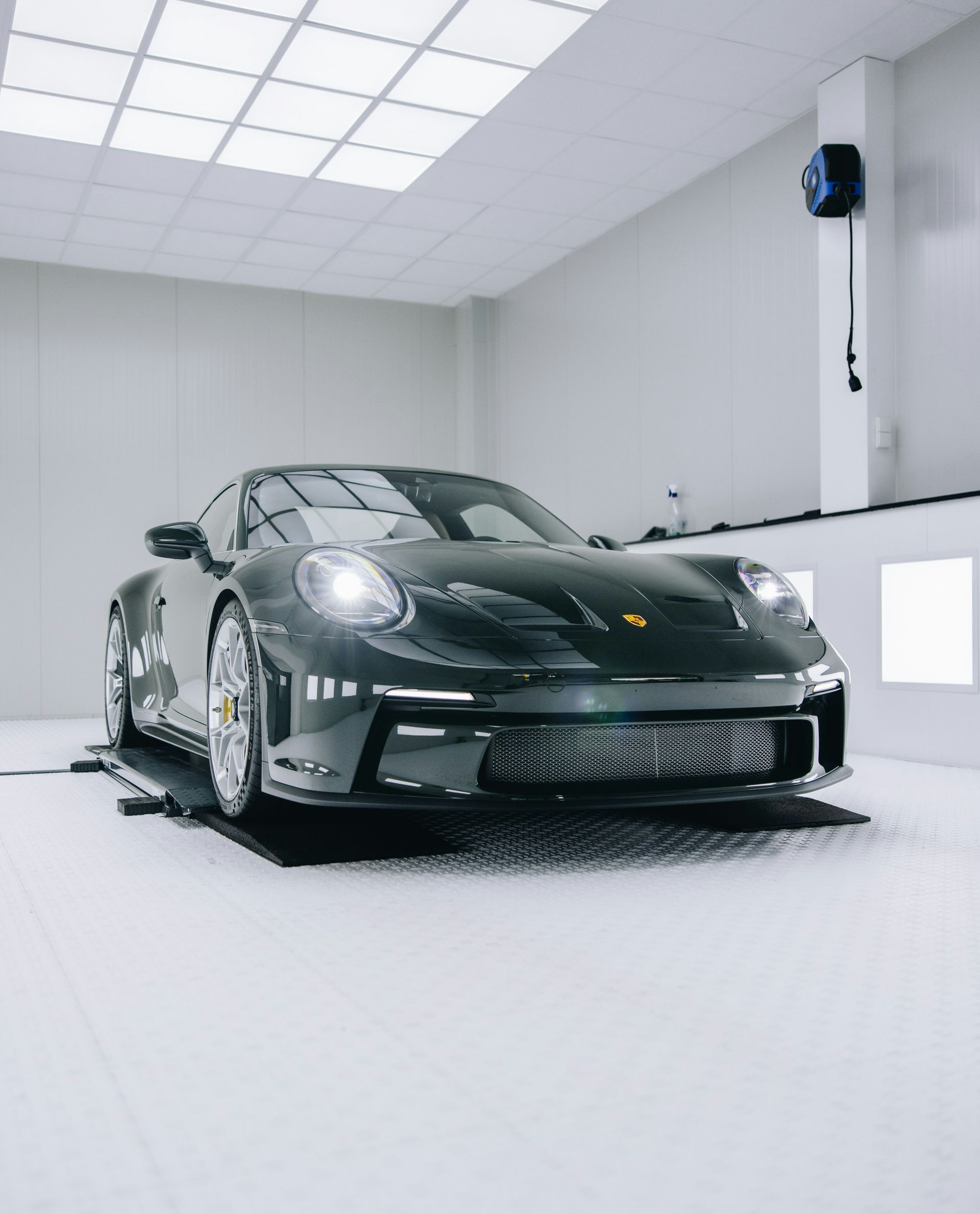 Dark gray Porsche 911 on a lift inside a white, well-lit garage.