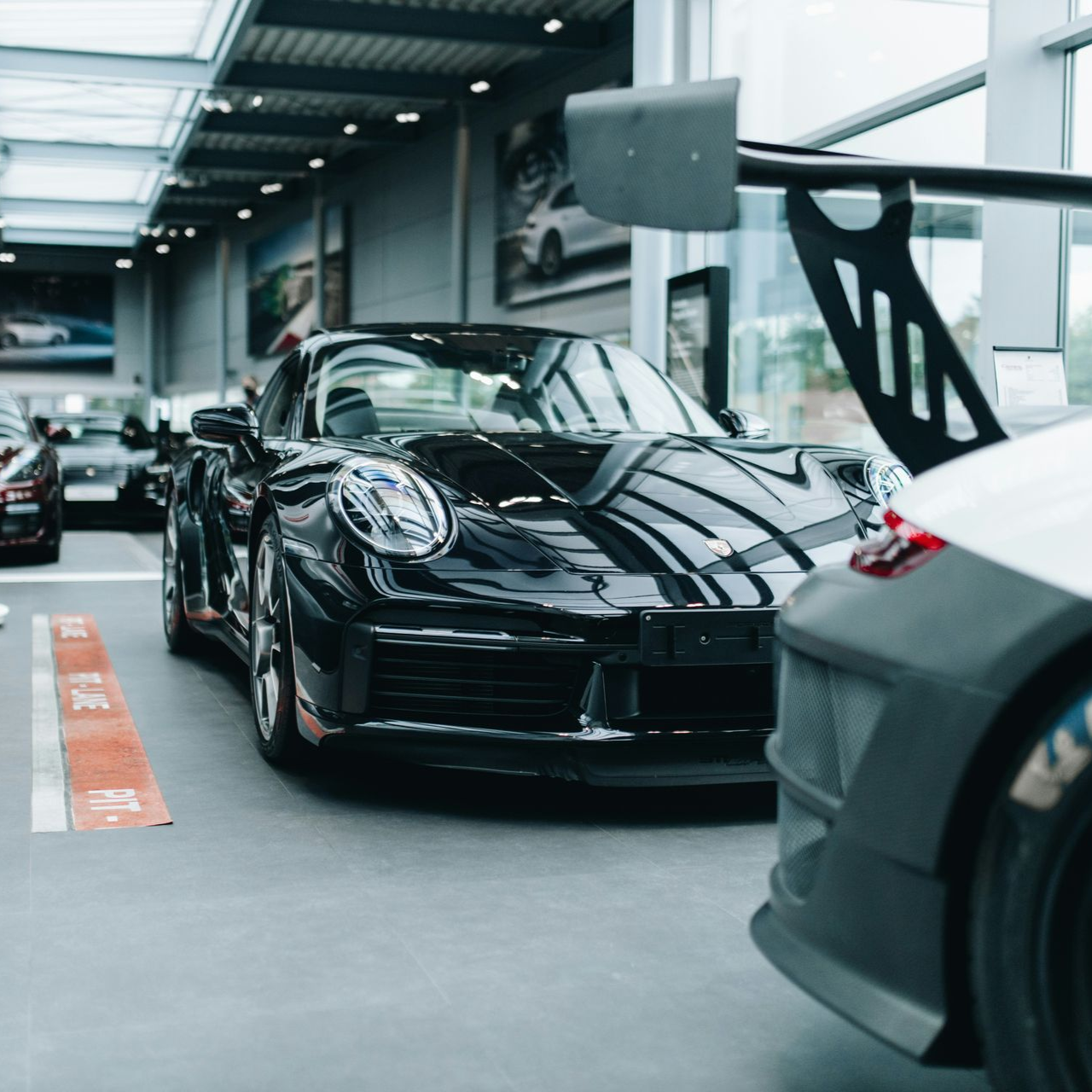 Black sports car in a showroom, with a white car in the foreground.