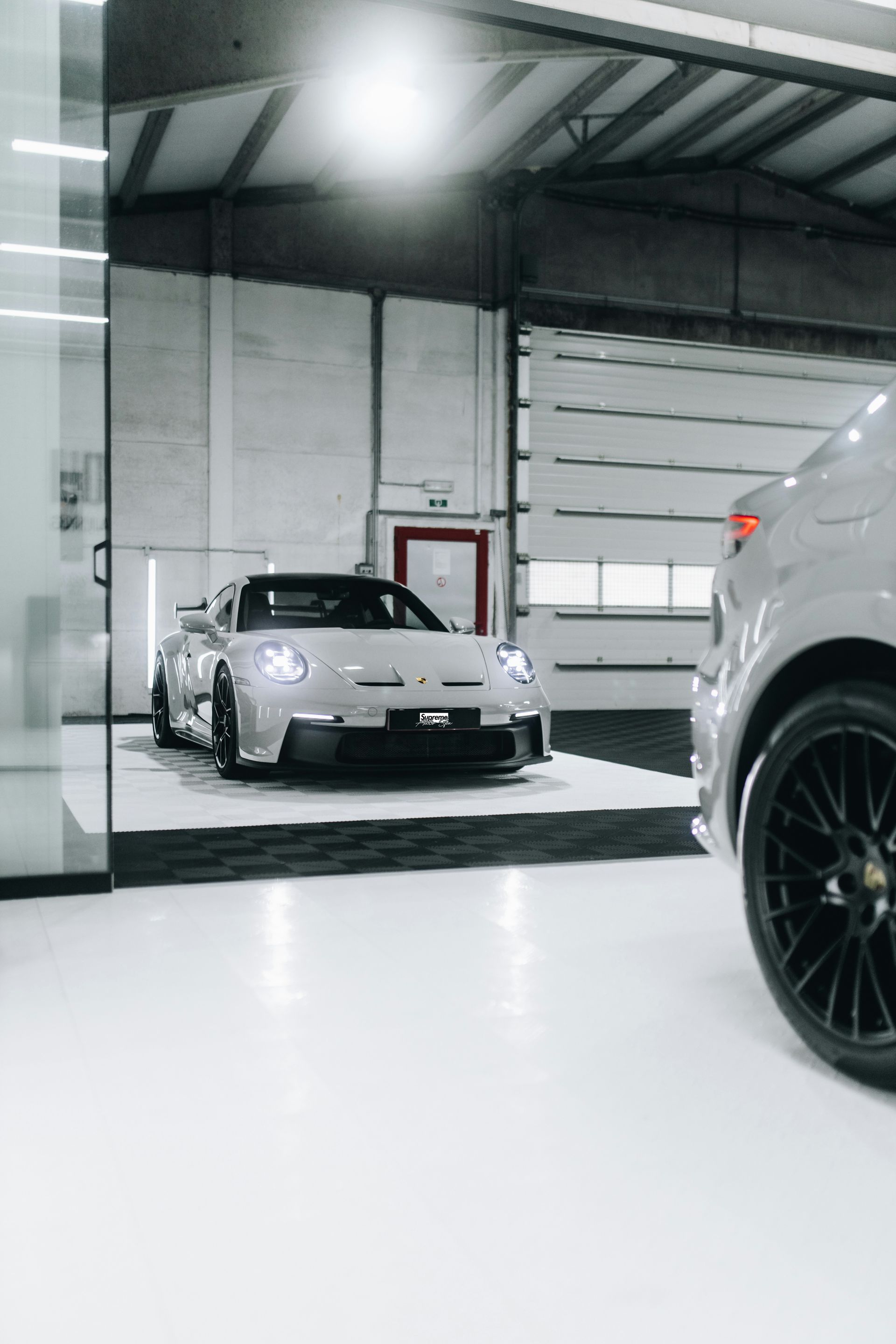 Silver sports car inside a garage, next to another car with a black wheel.