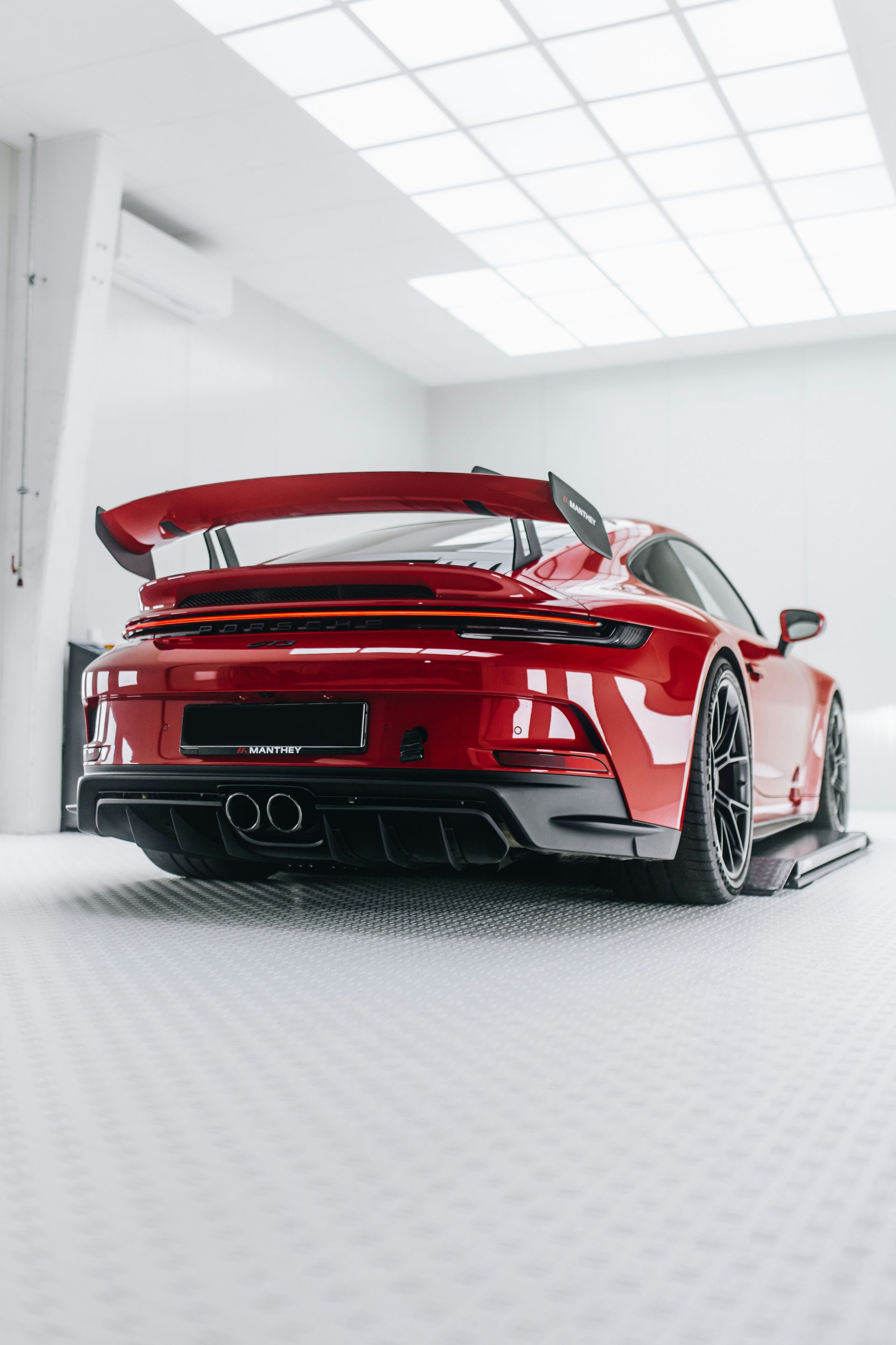 Red Porsche 911 GT3 with large rear wing, in a bright white studio, rear view.