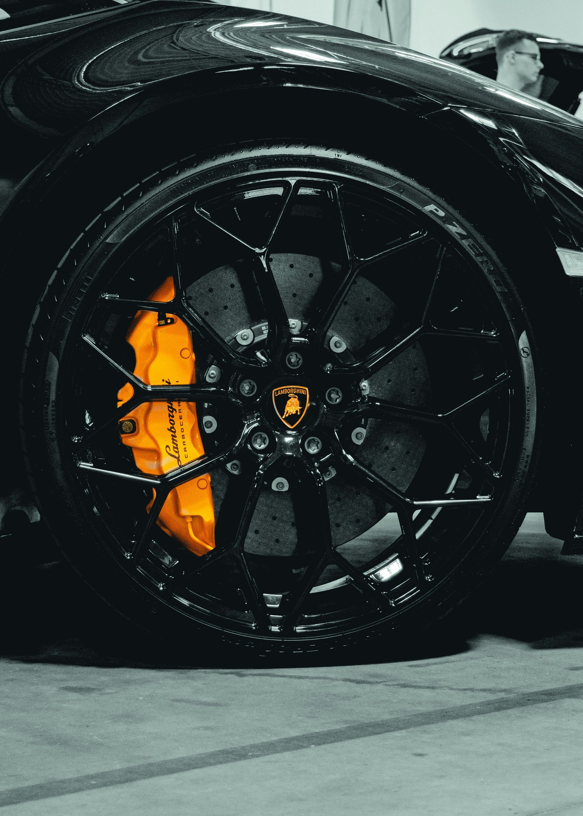 Black Lamborghini wheel with orange brake caliper and Lamborghini logo.