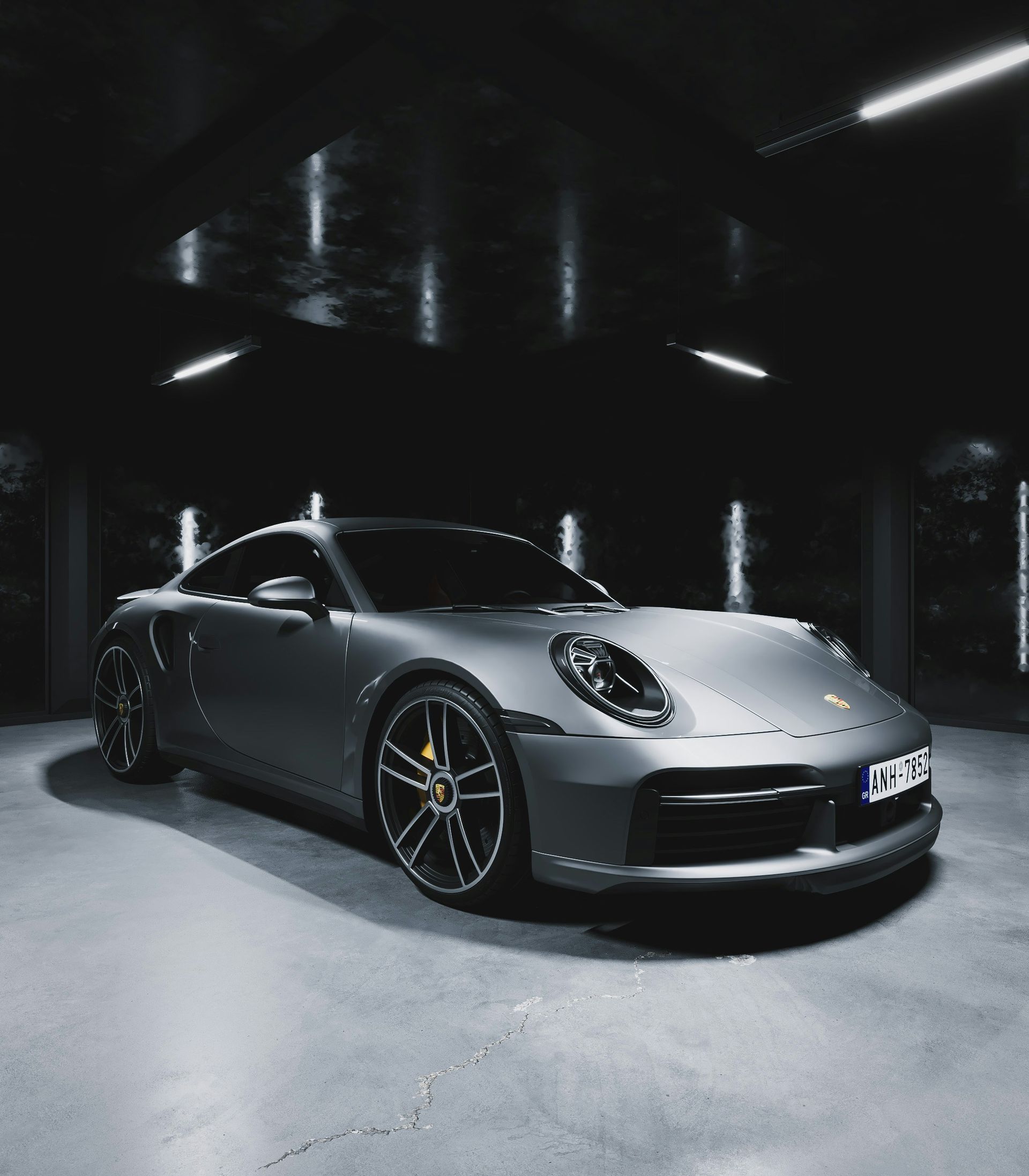 Gray Porsche 911 sports car parked inside a dimly lit garage with overhead lights.