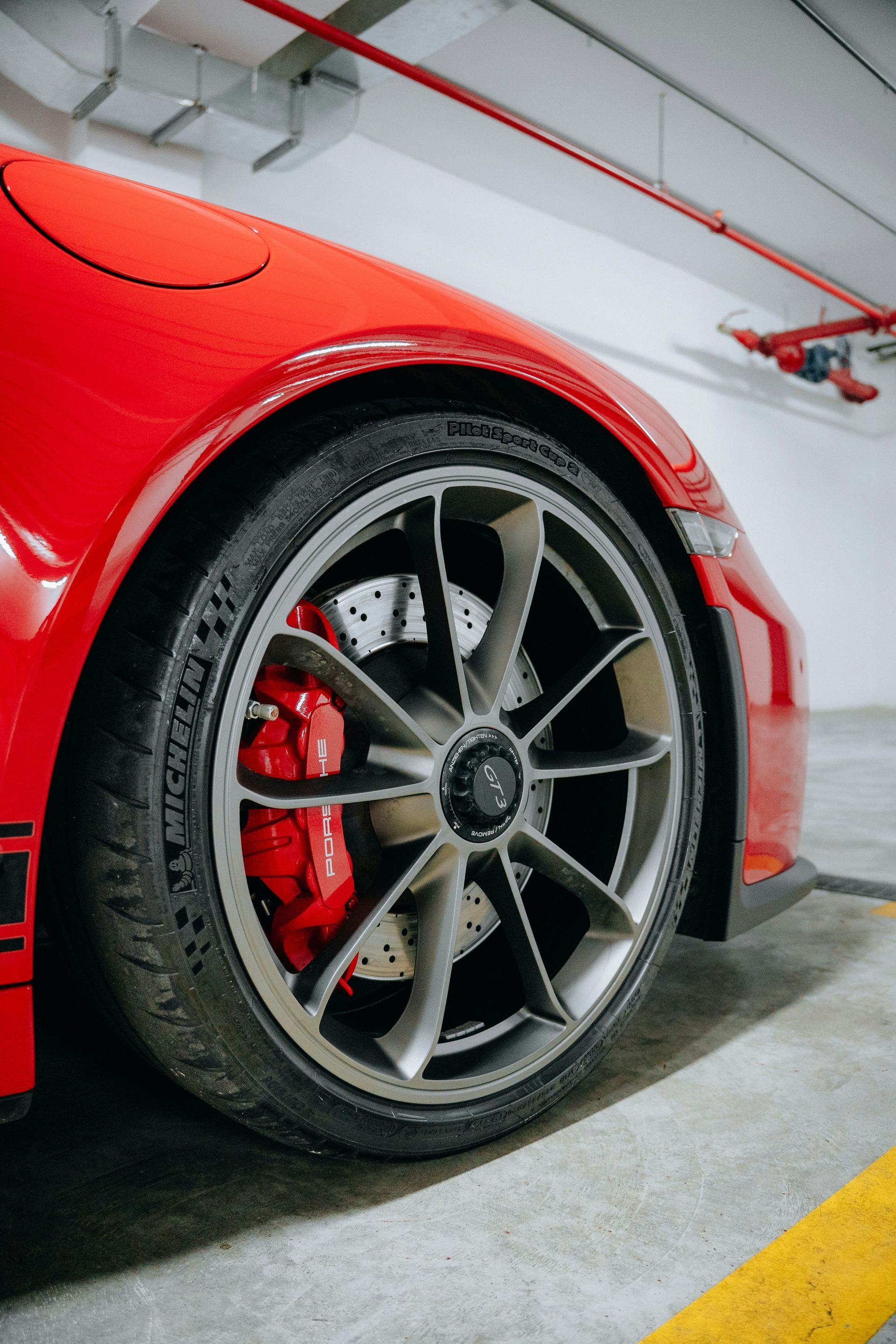 Red Porsche sports car, front tire and wheel, parked in a garage.