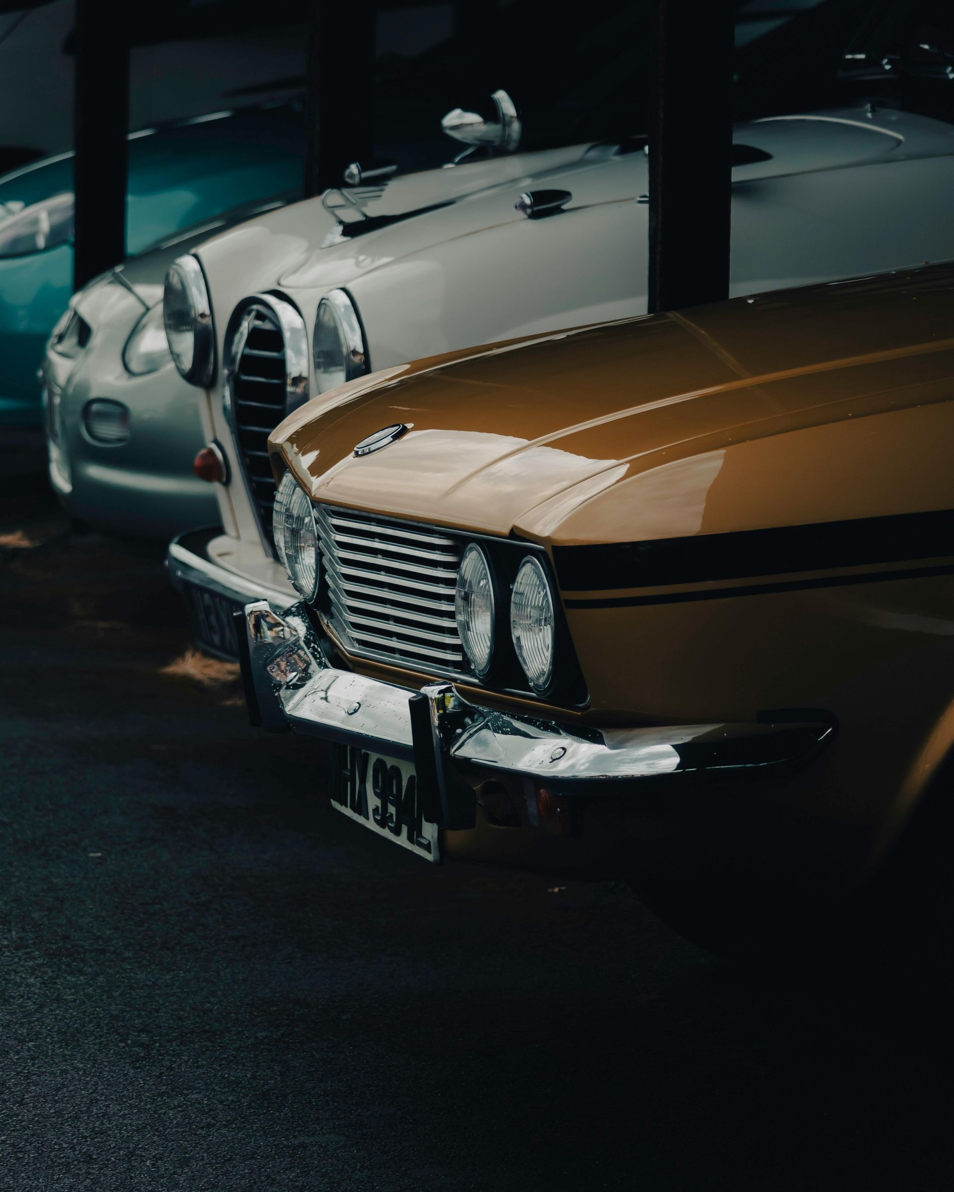 Classic yellow car parked next to two other vintage cars in a dark garage.