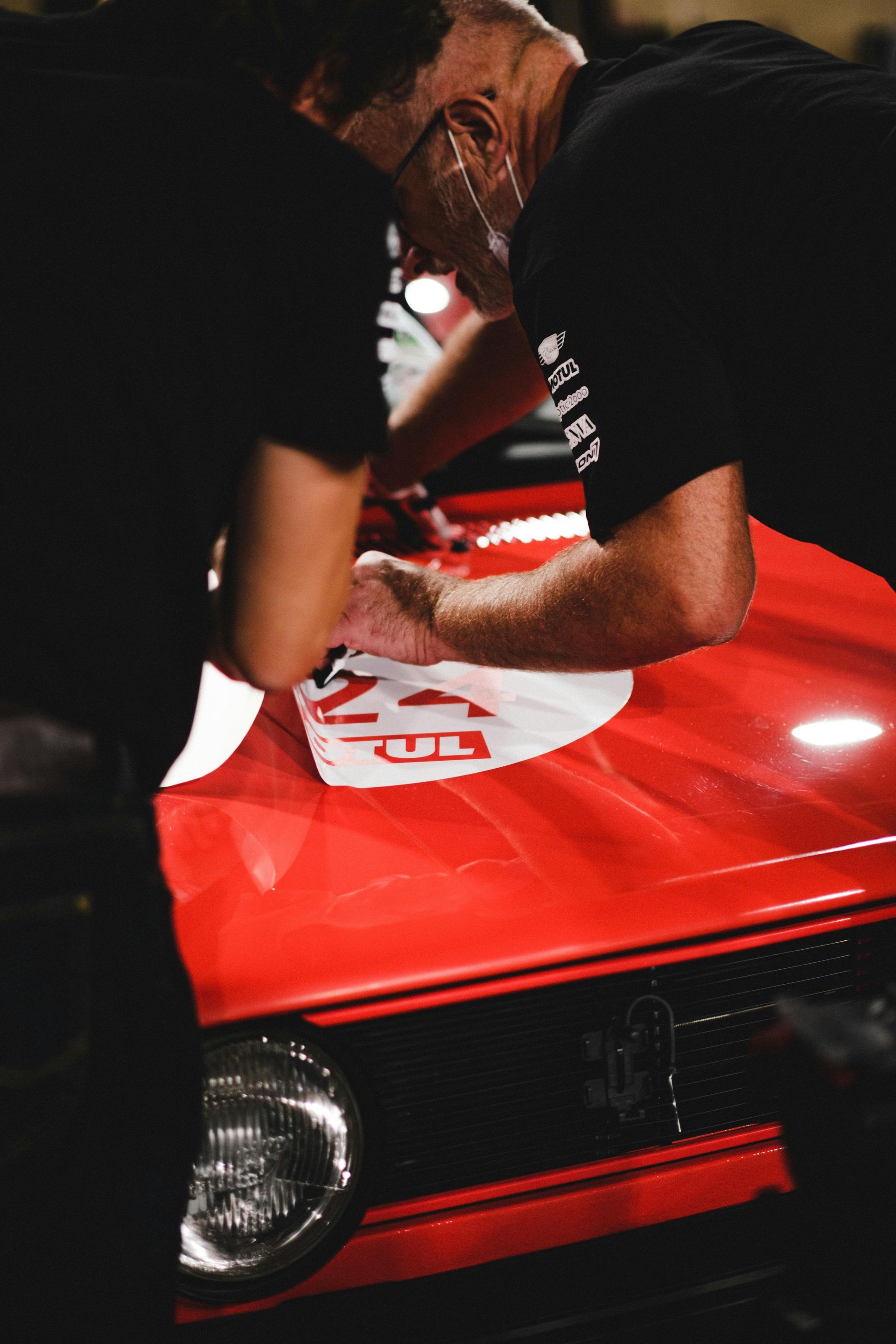 Two people applying a sticker to the red hood of a car.