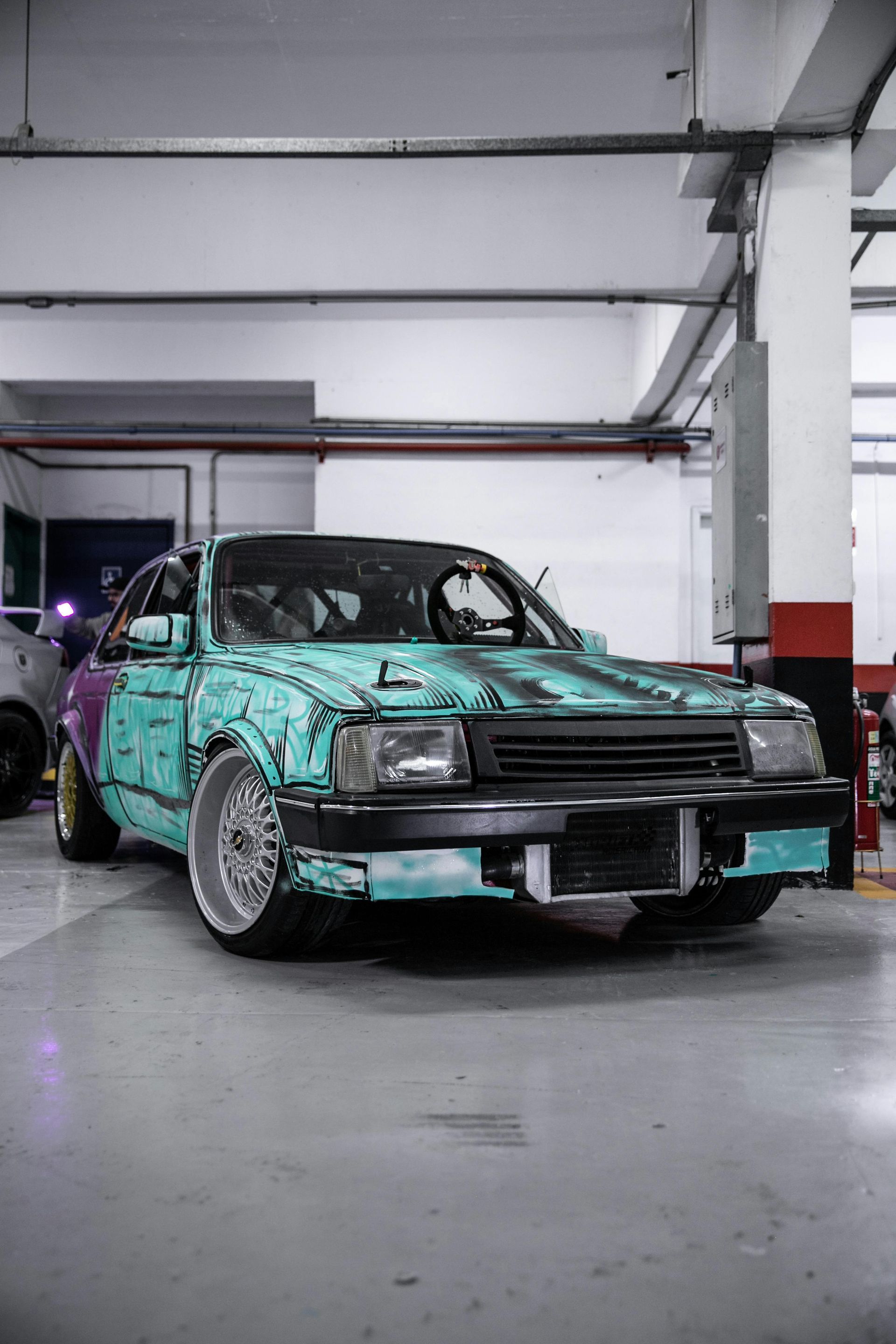 Modified, turquoise, compact car with gold wheels, in a garage setting.