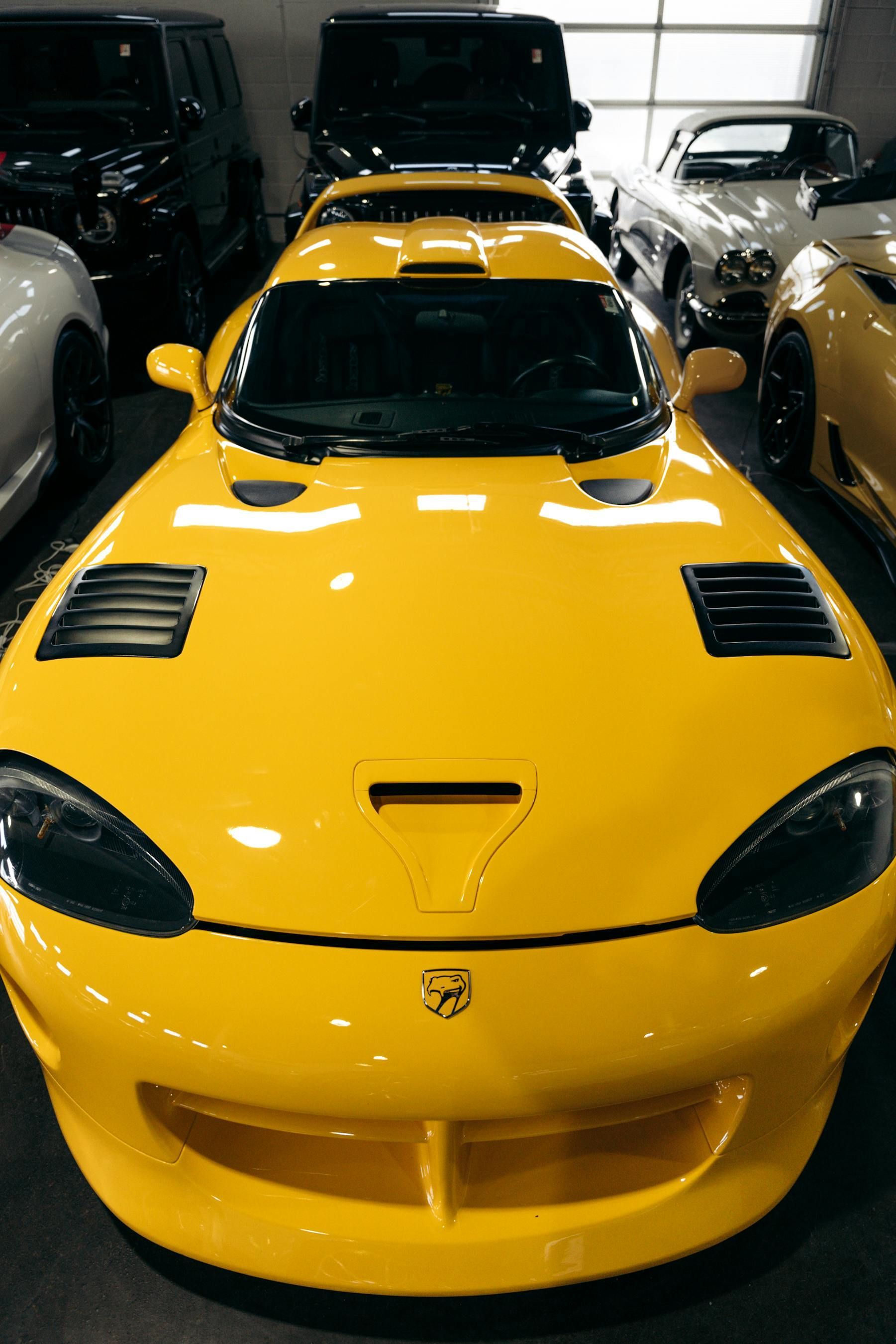 Yellow Dodge Viper sports car, surrounded by other vehicles, indoors.