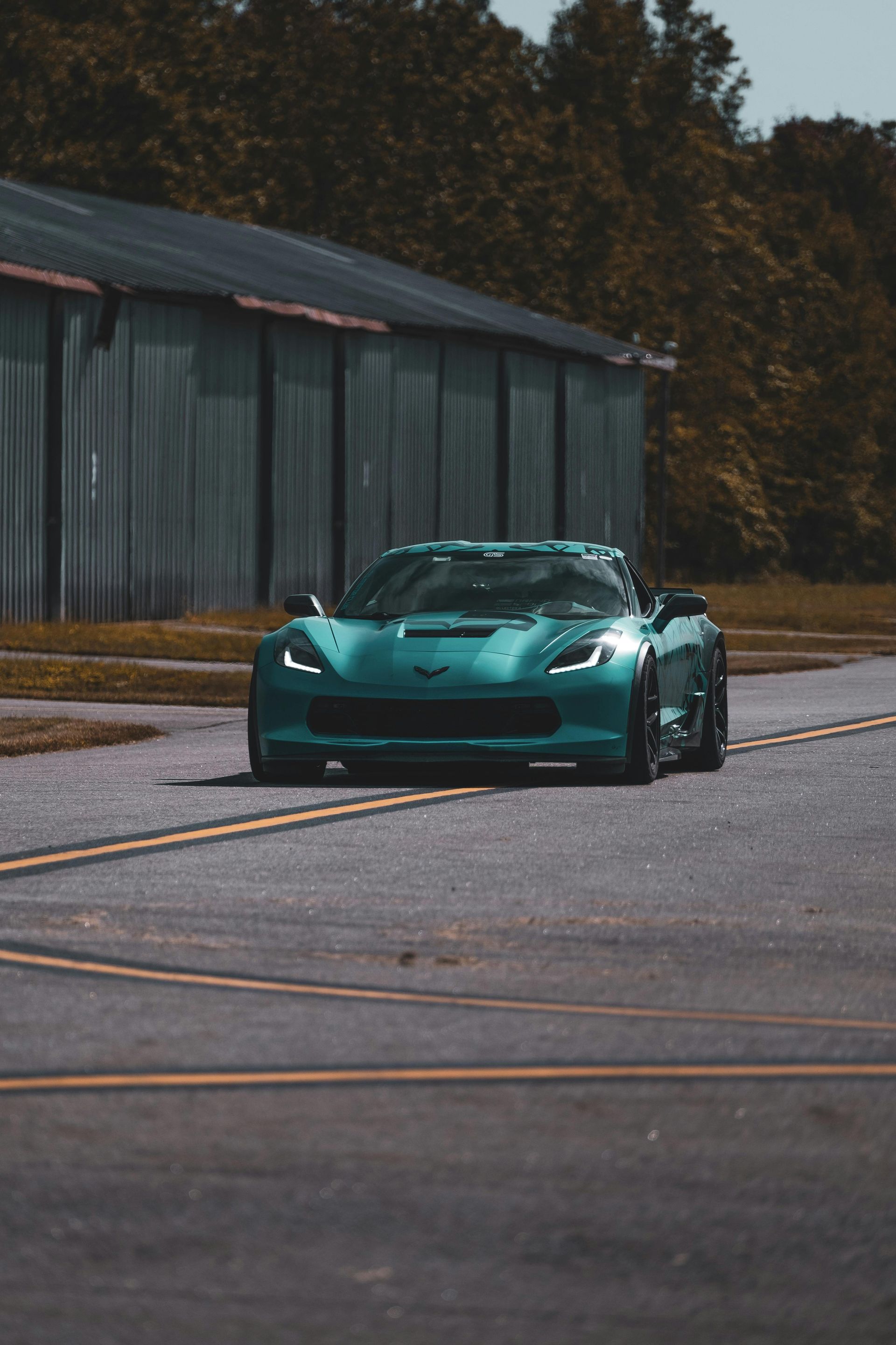 Green Corvette sports car driving on a road near a building with an overcast sky.