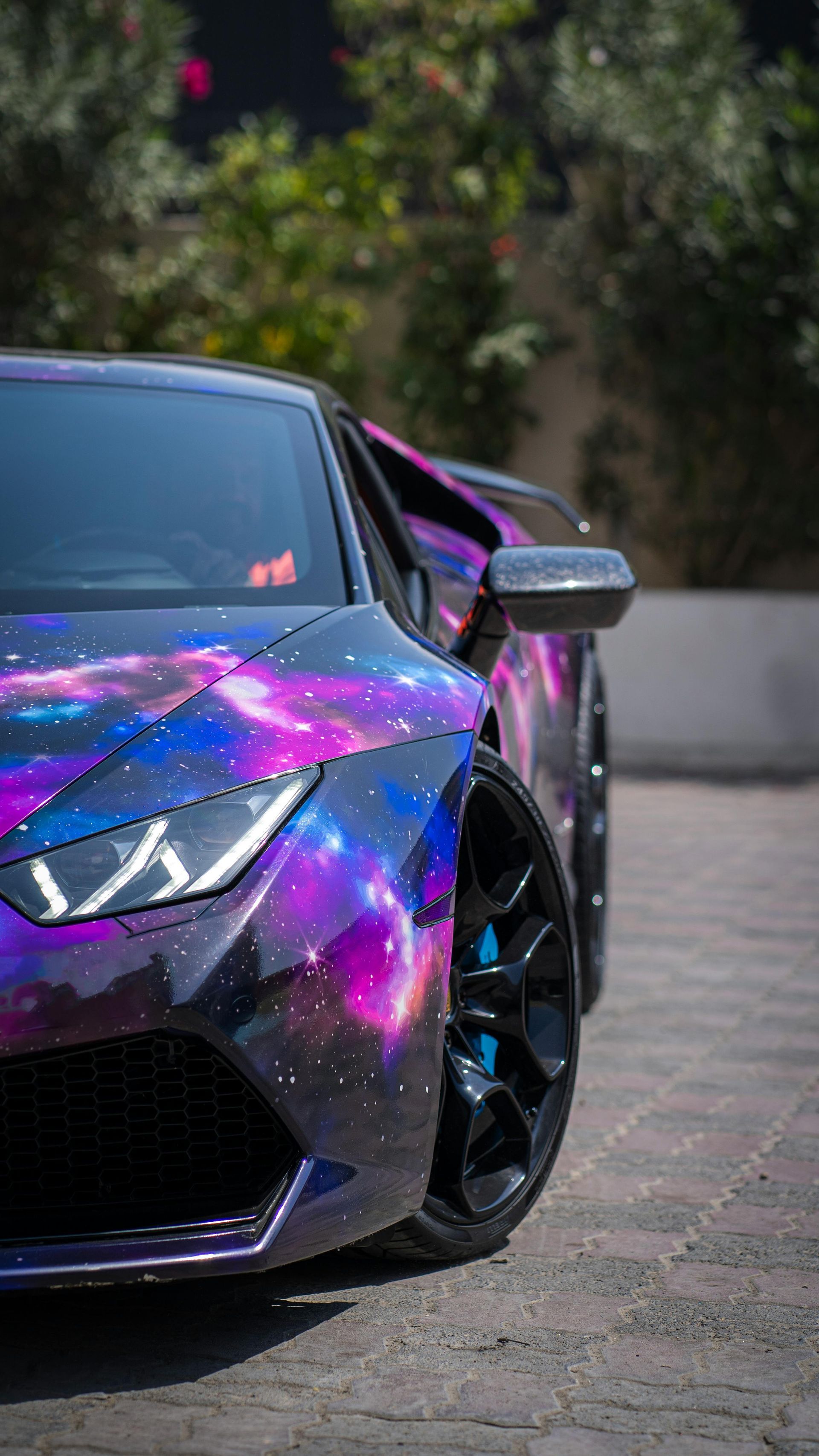 A custom galaxy-wrapped Lamborghini sports car parked outside, with a colorful cosmic design.