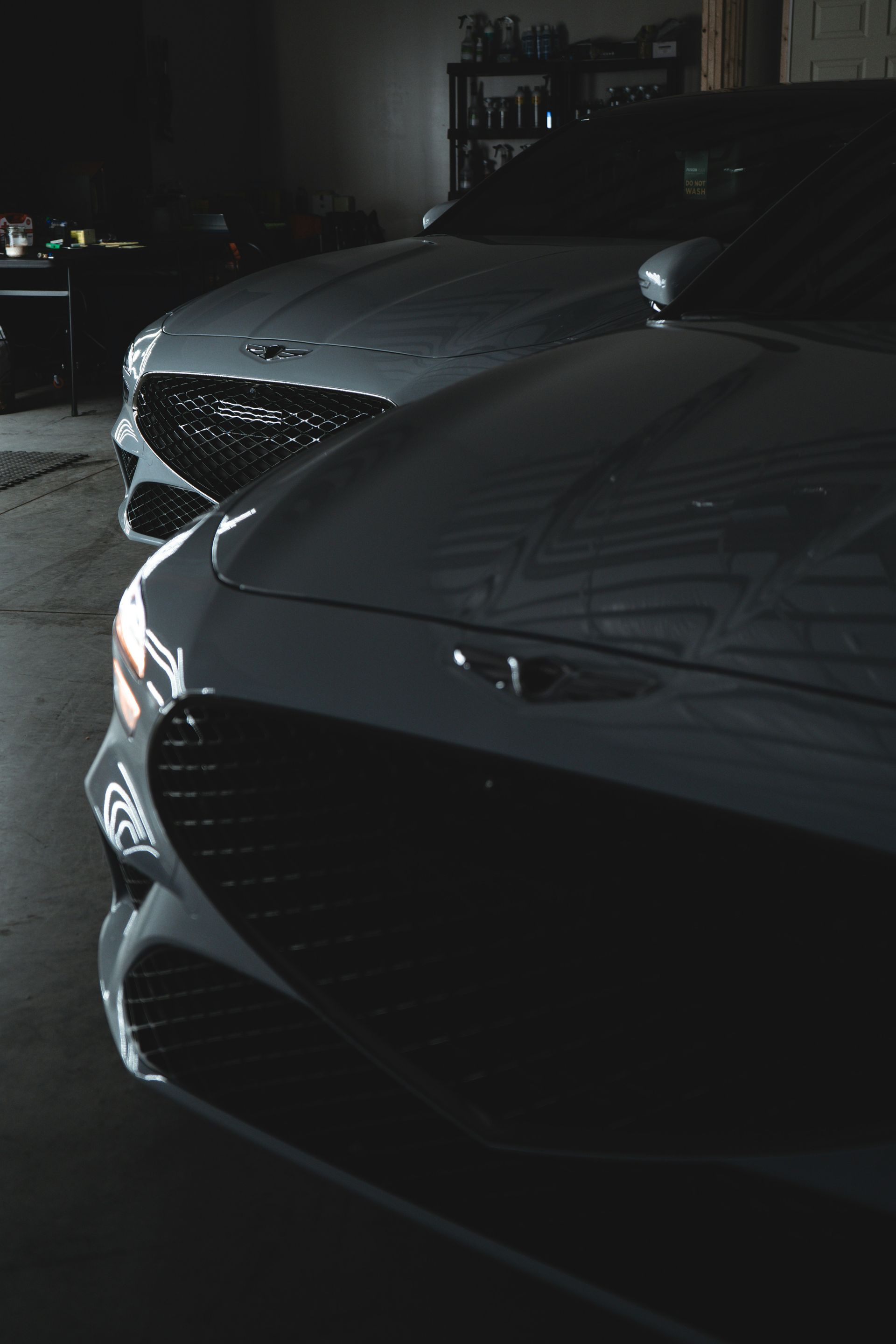 Two gray luxury cars parked side-by-side in a dimly lit garage, front ends visible.
