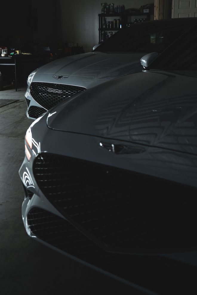 Two gray luxury cars parked side-by-side in a dimly lit garage, front ends visible.