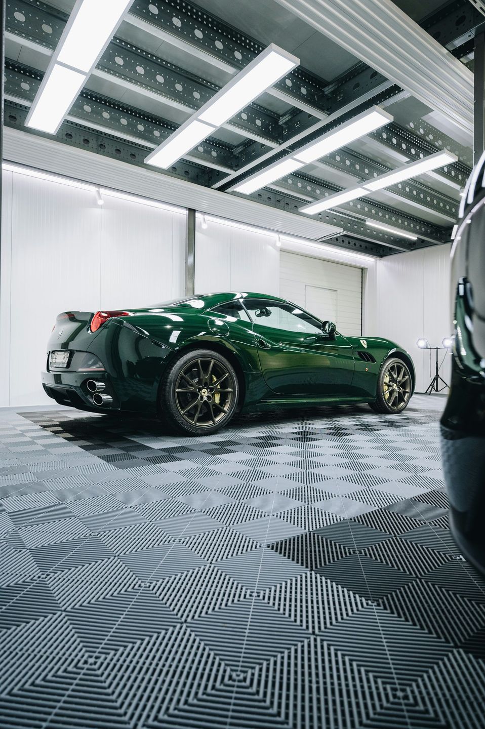 Green sports car in a brightly lit garage, detailed black wheels, and a patterned floor.