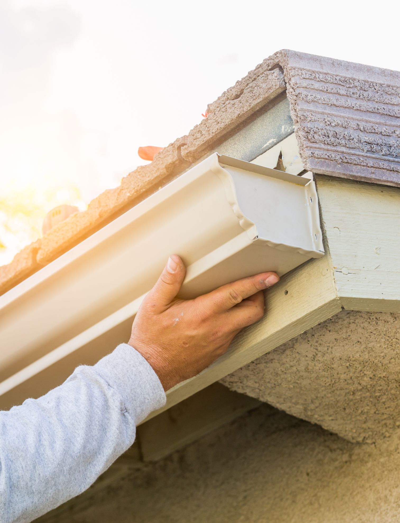 A man is installing a gutter on the side of a house.