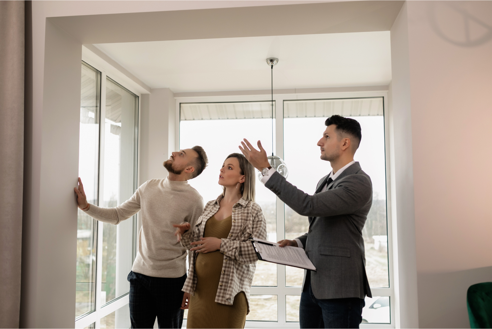 Real estate agent showing a couple a room with large windows, gesturing toward the view.
