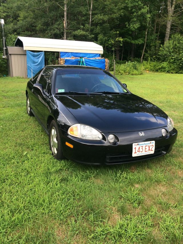 Black sedan parked on grass in front of a tarp-covered shed and trees | Village Repair
