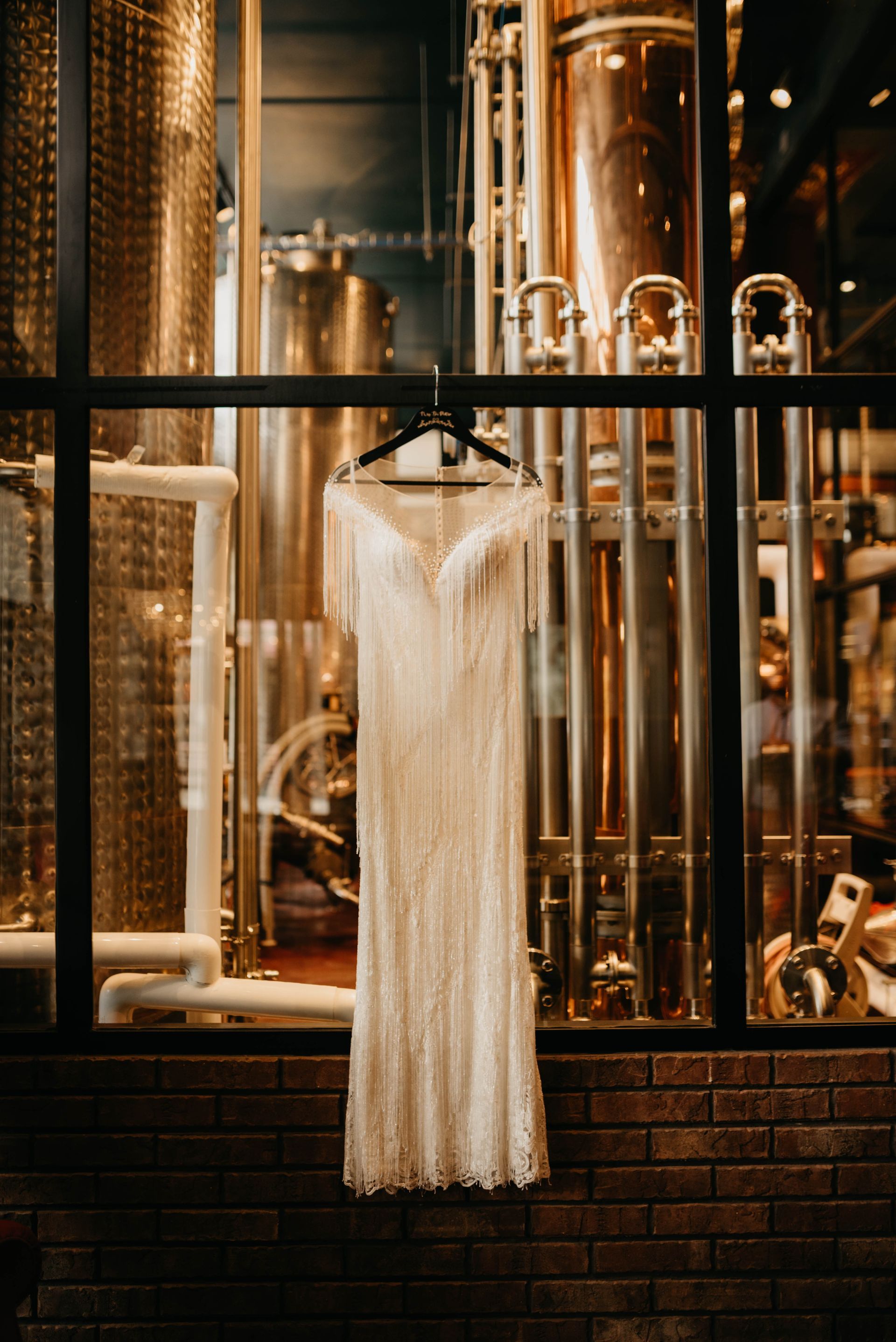 a wedding dress hangs in front of a window in a brewery