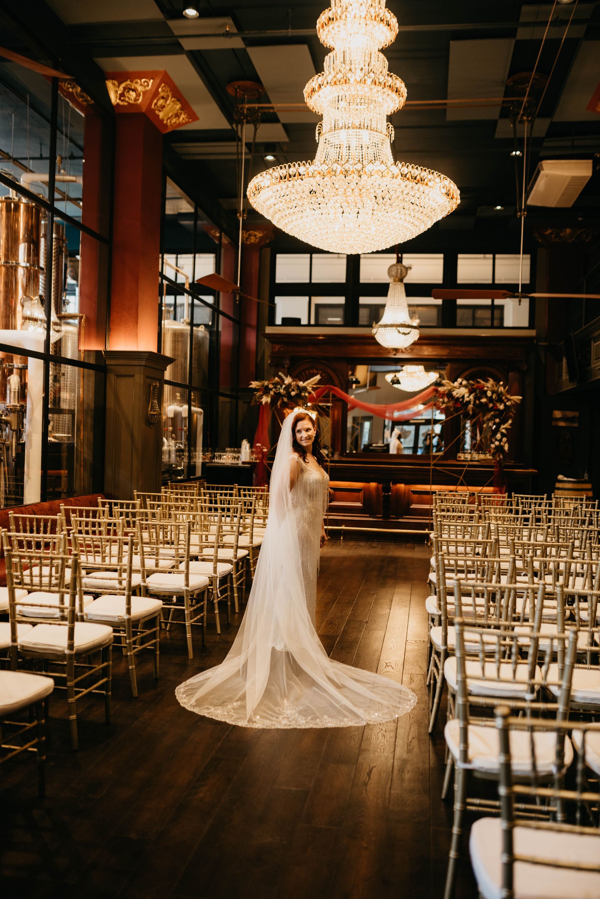 a bride stands in front of rows of chairs under a chandelier