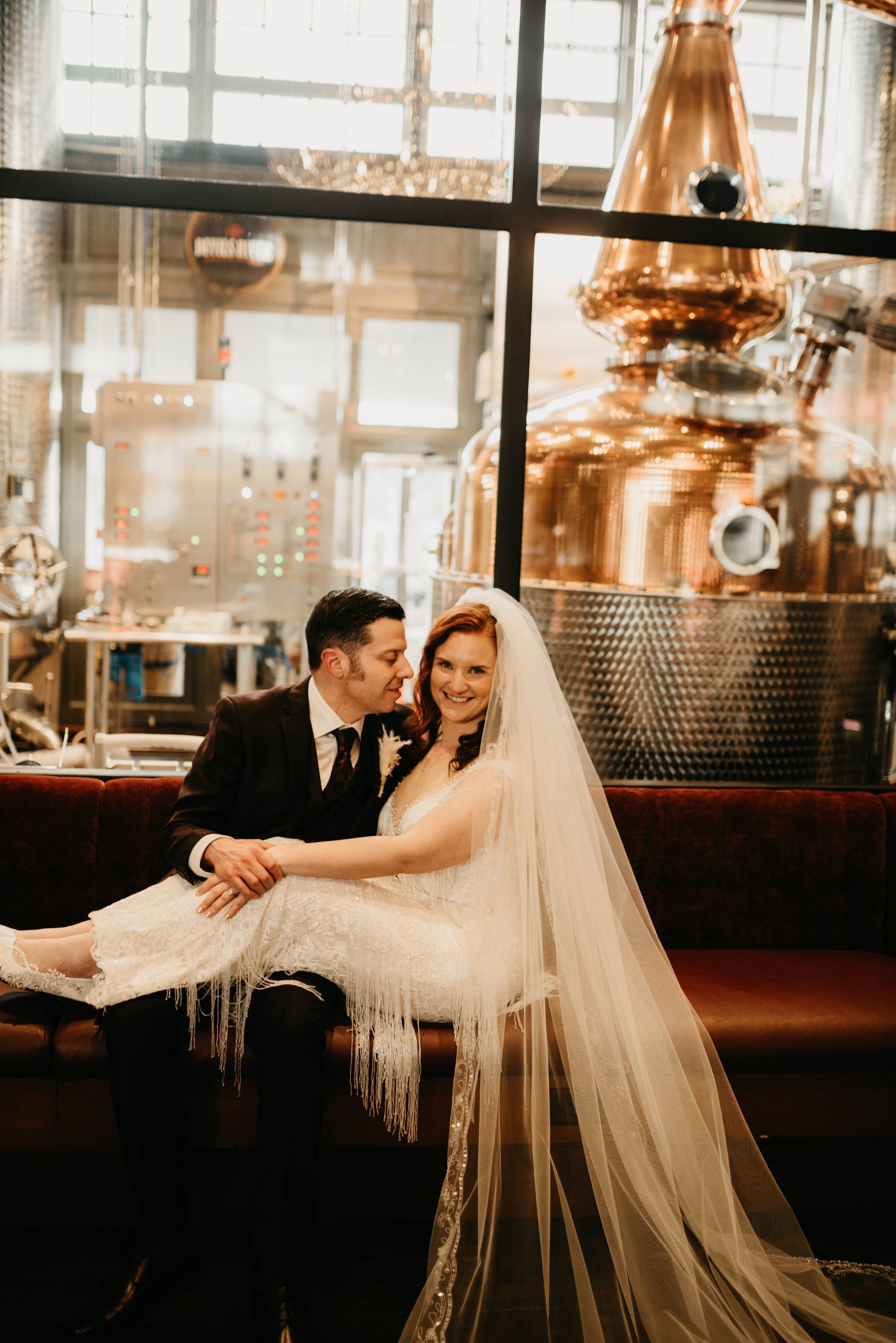a bride and groom sit on a couch in front of a distillery