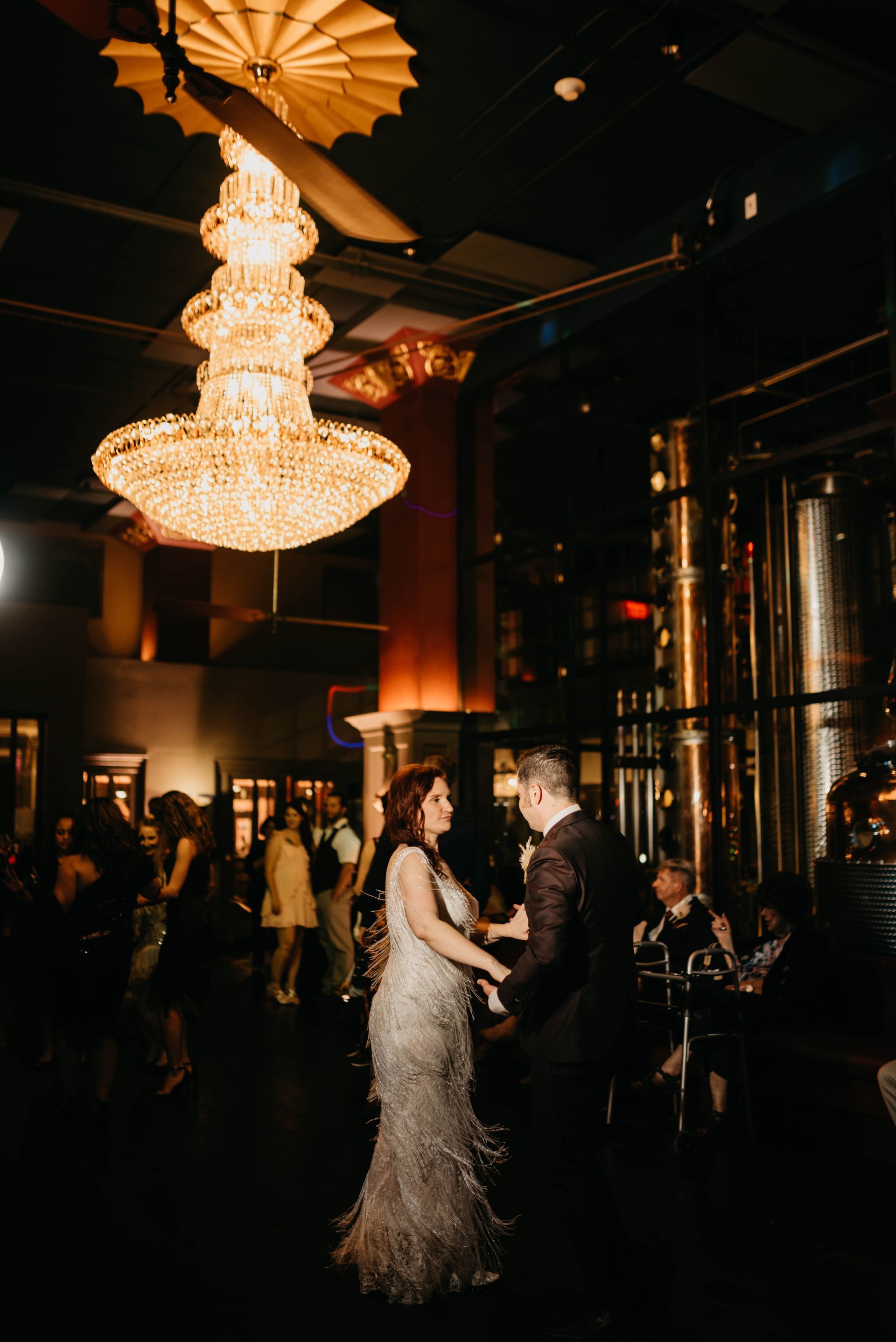 a bride and groom are dancing under a large chandelier