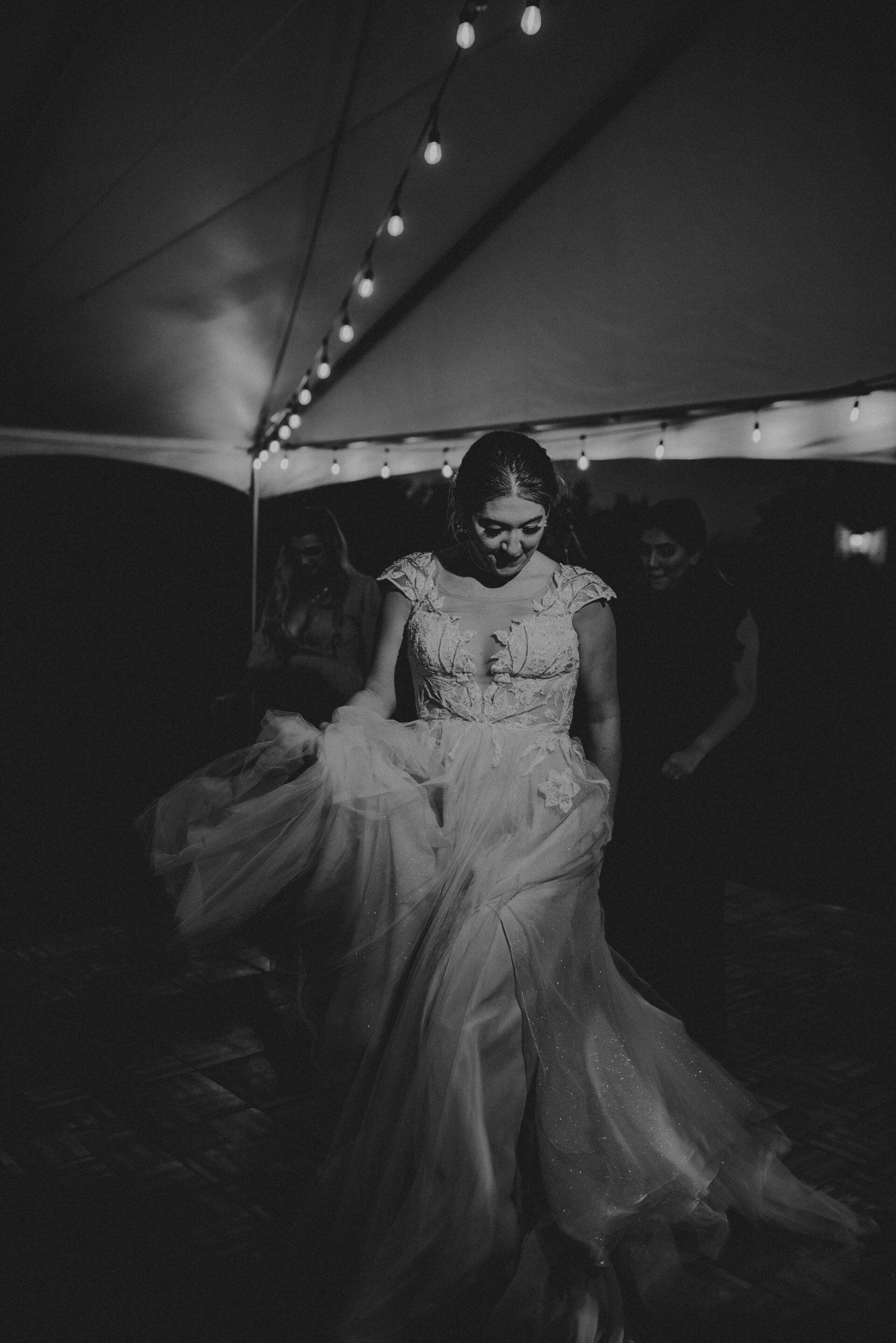 a woman in a wedding dress is dancing under a tent