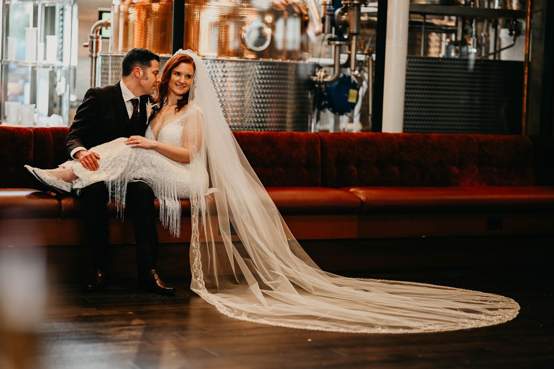 a bride and groom are sitting on a couch and the bride is wearing a long veil